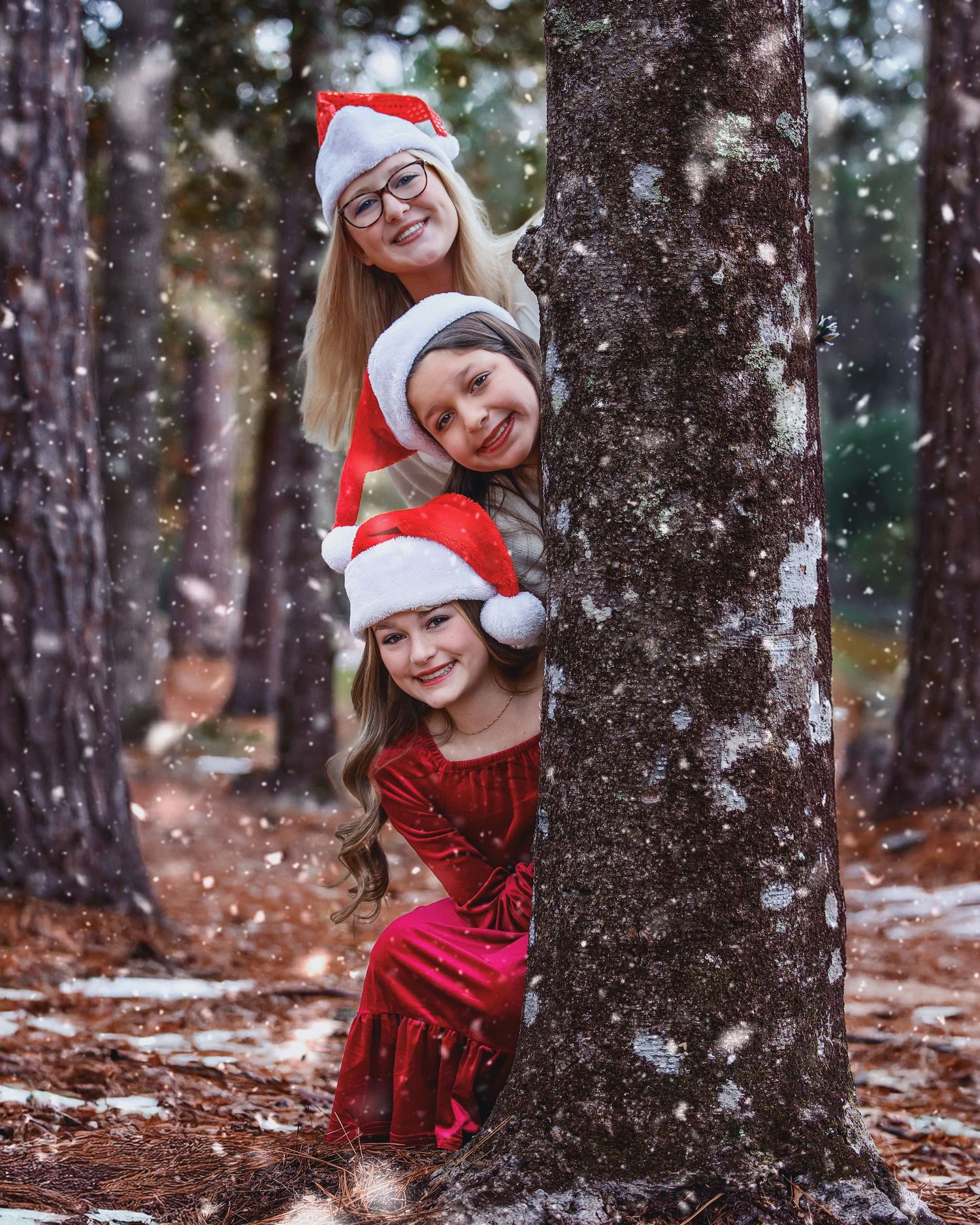 Playful holiday portraits peeking around snowy trees while wearing a Santa hat and red dress.