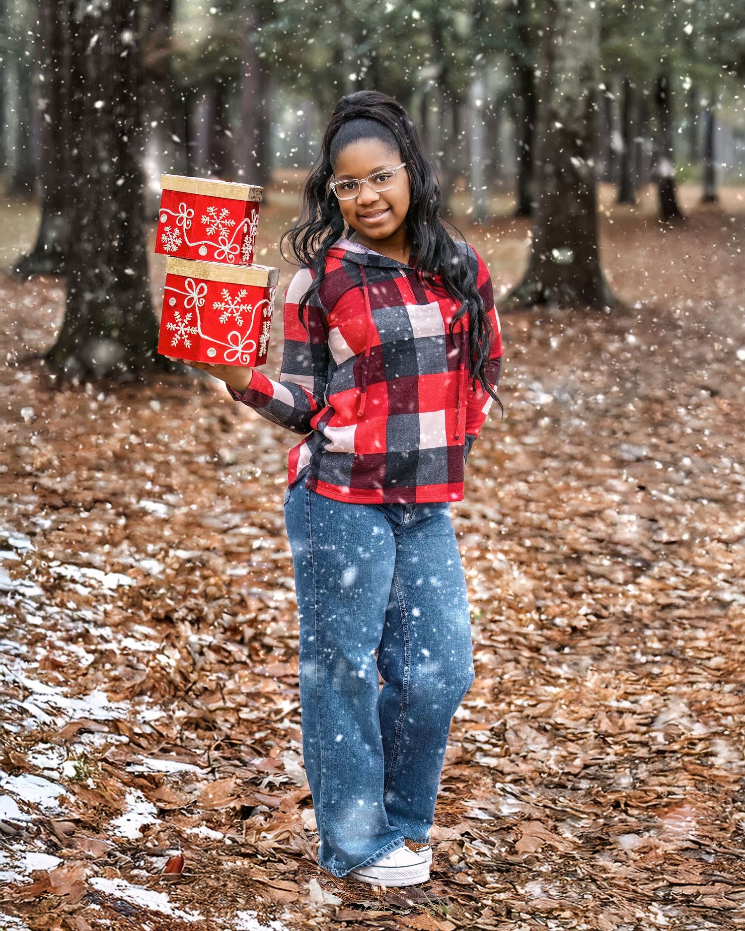 Person wearing red plaid jacket and jeans poses playfully in falling snow among scattered autumn leaves.