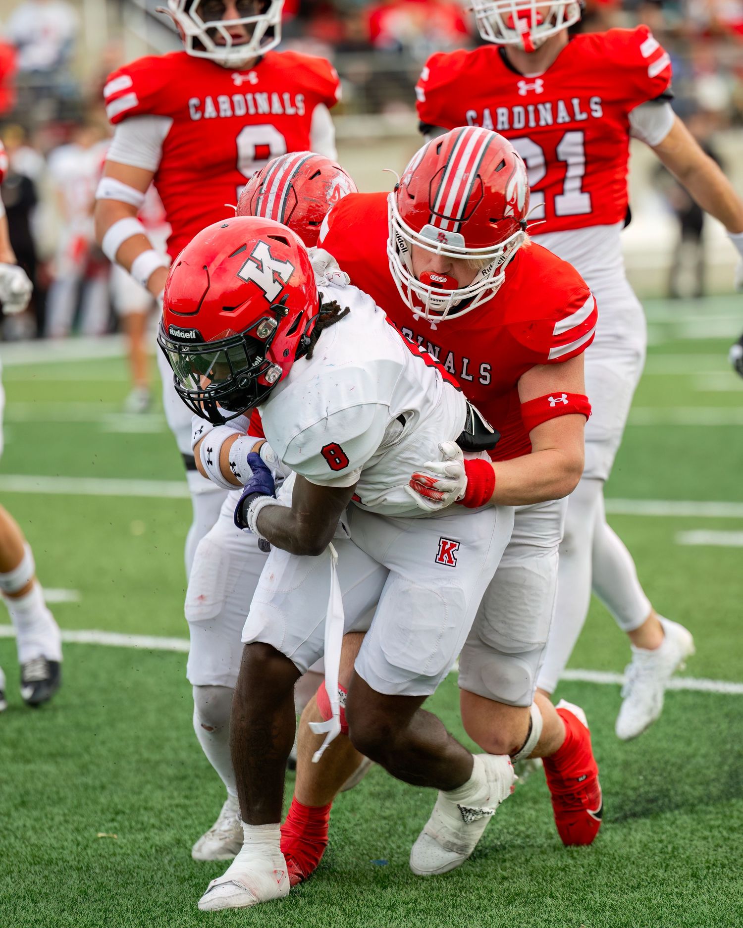 High School Senior Football players in red and white uniforms engage in ground-level action during a game.