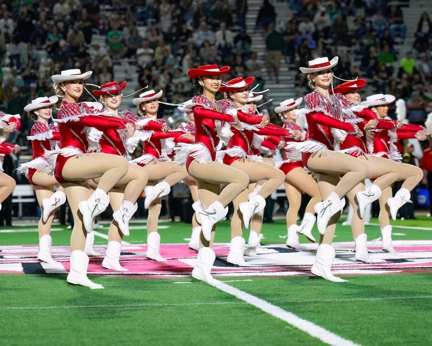 A line of cheerleaders performing a synchronized kneeling routine on the football field.