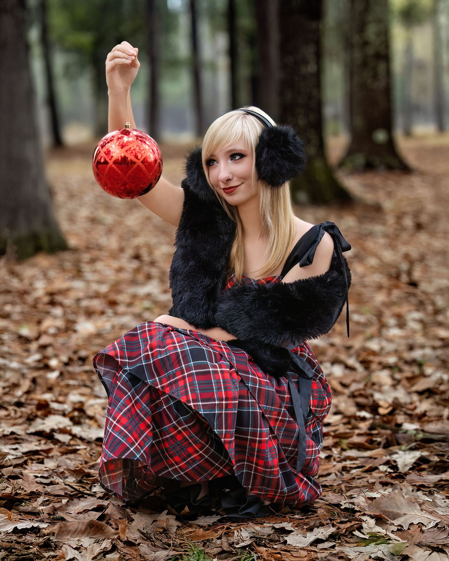 Jaylin  in a plaid dress lies on autumn leaves in a forest setting.