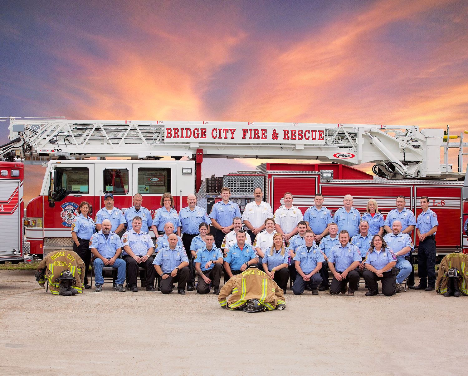 Bridge City Texas Firefighters in blue uniforms pose in front of red fire trucks and equipment during sunset at a fire station.