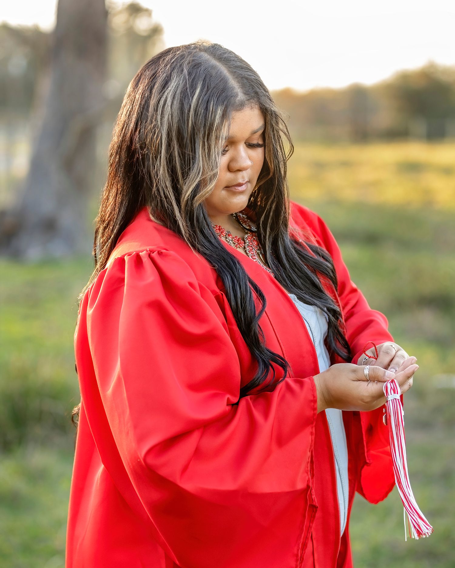 A person in a bright red graduation gown laughs and smiles during an outdoor photoshoot at sunset.