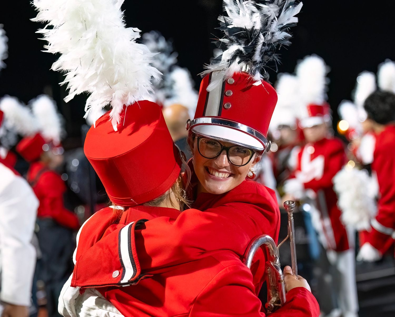 Members of a marching band wearing red uniforms and white plumes perform during a parade or event.