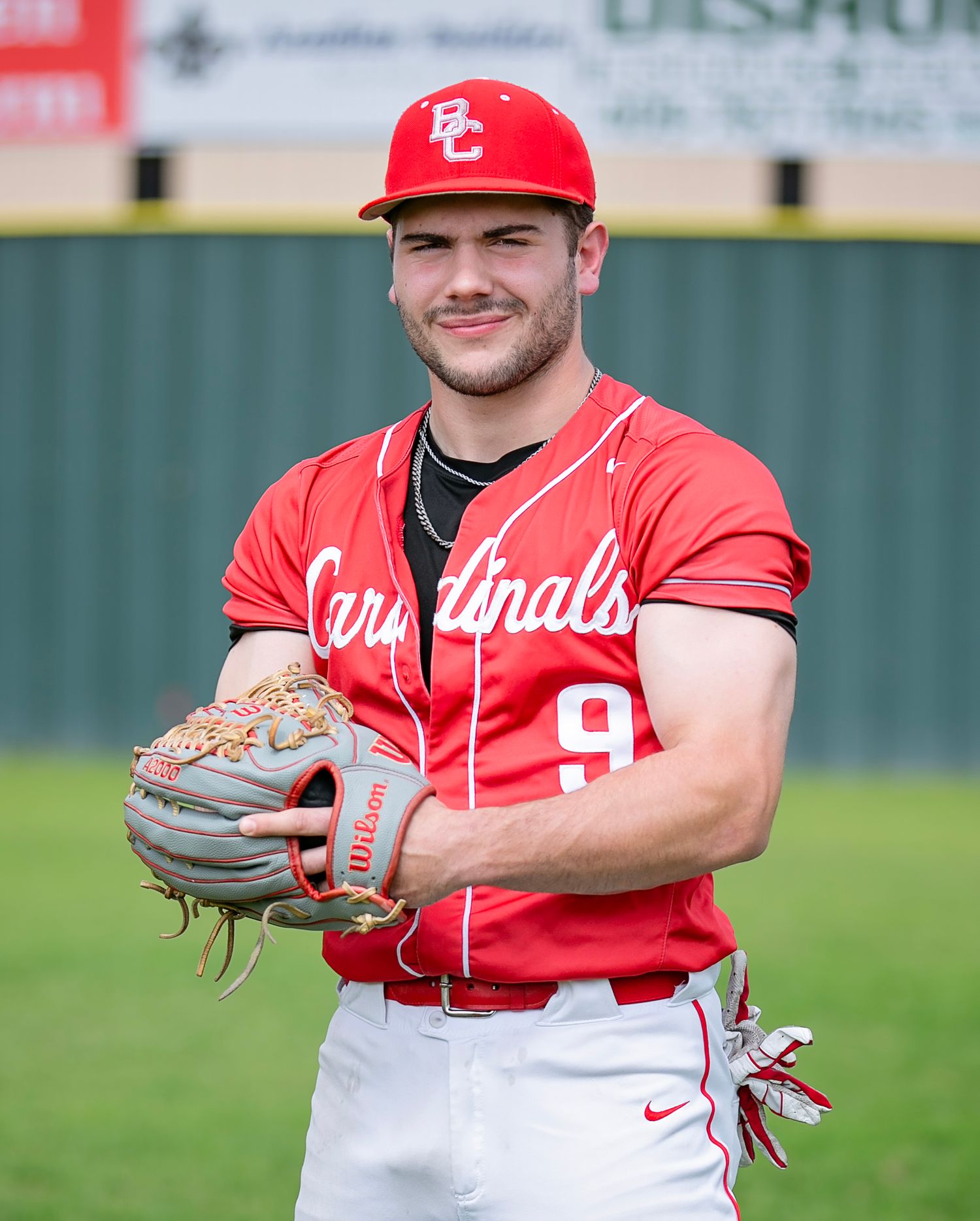 Baseball player in red Cardinals jersey and cap smiles while holding a glove on the field.