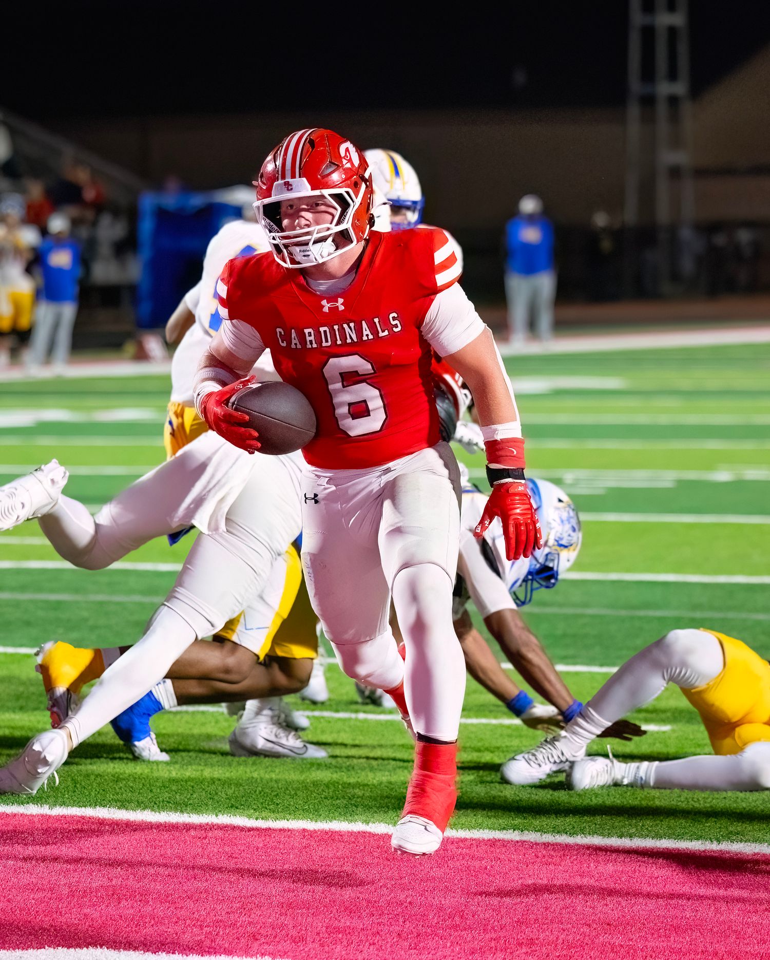 Football players in red and white uniforms dive for the ball during intense game action.