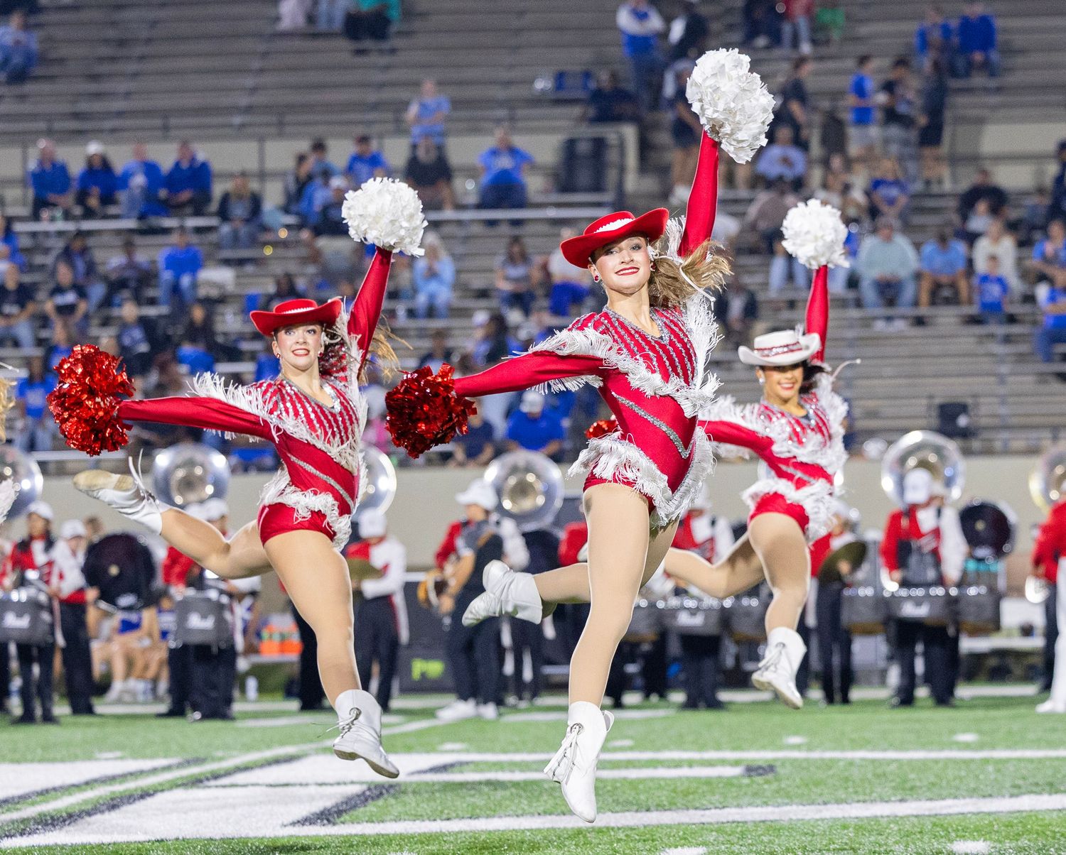 Cheerleaders perform synchronized splits during a football game with stadium crowd in background.