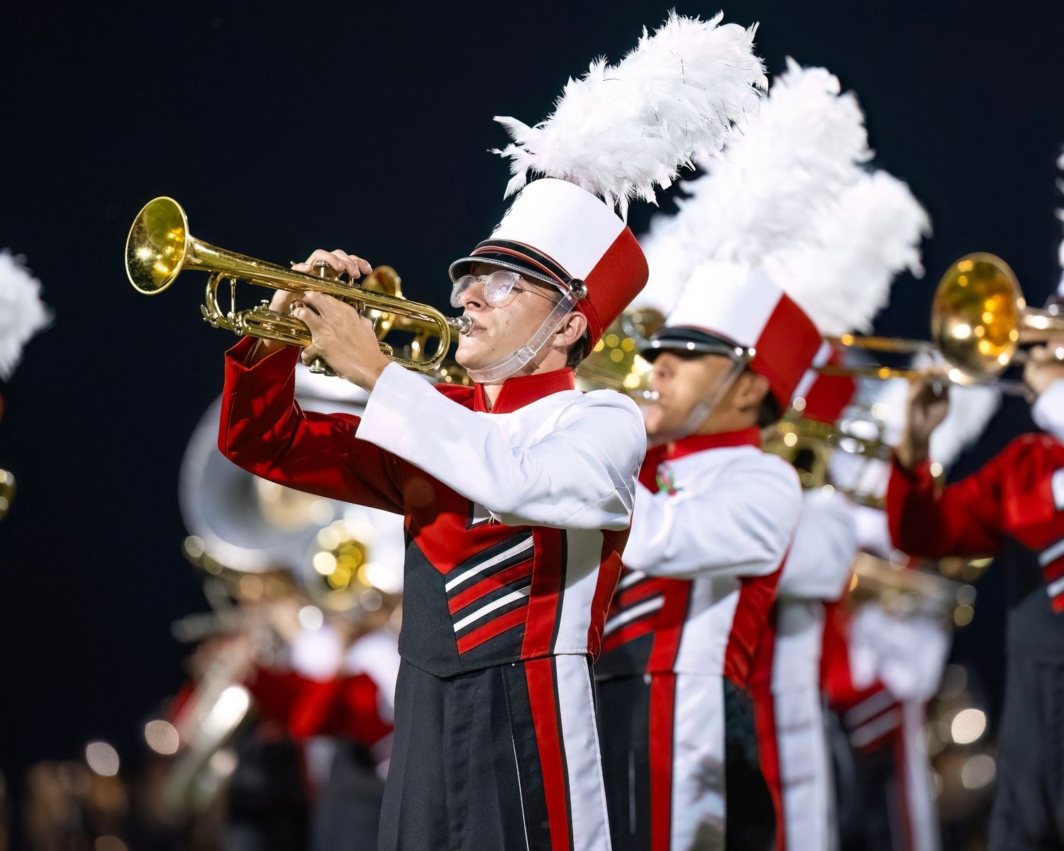 Line of marching band members playing brass instruments in red and white uniforms.