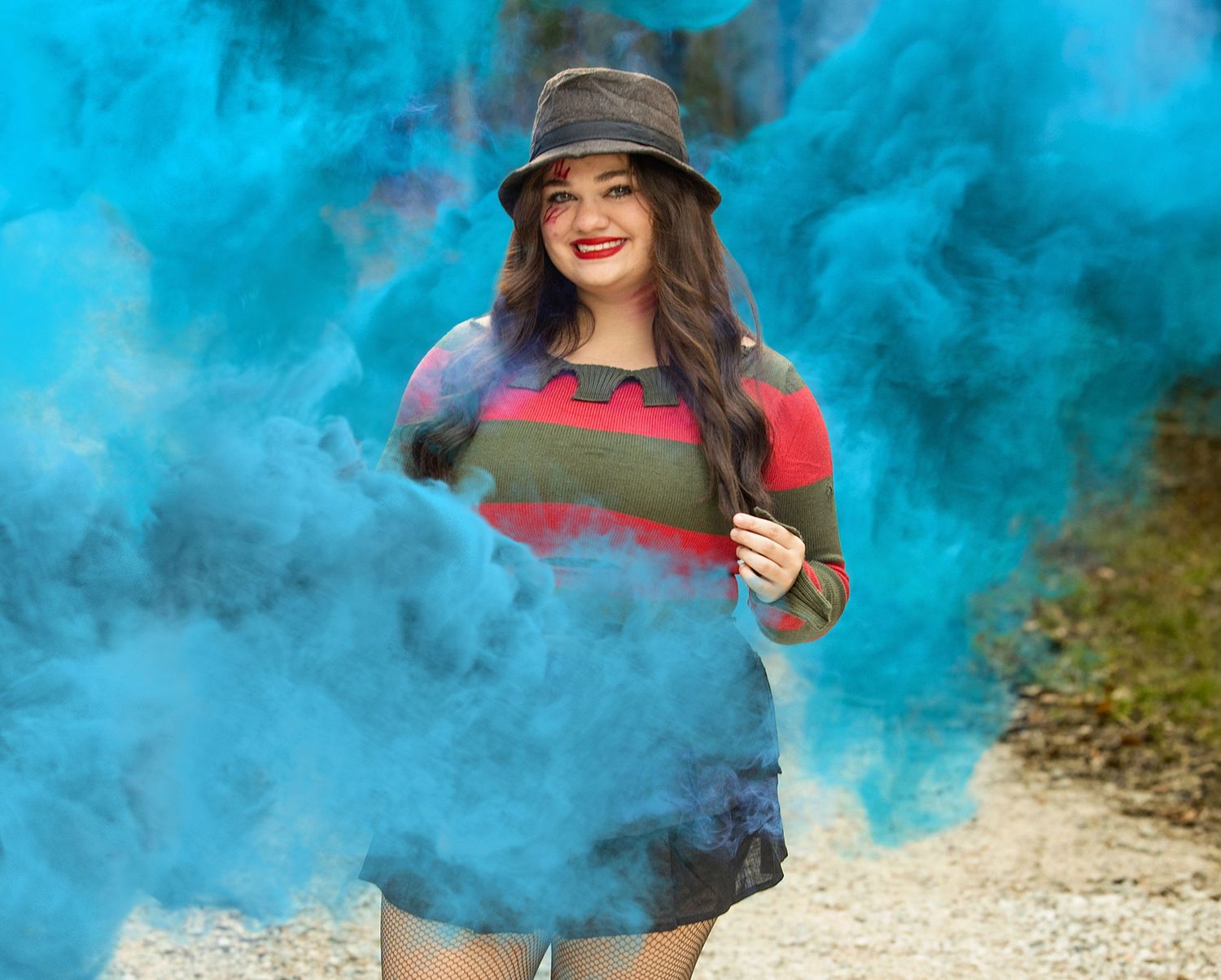 Eisley poses with vibrant blue smoke bombs creating an ethereal atmospheric effect against a natural outdoor backdrop.