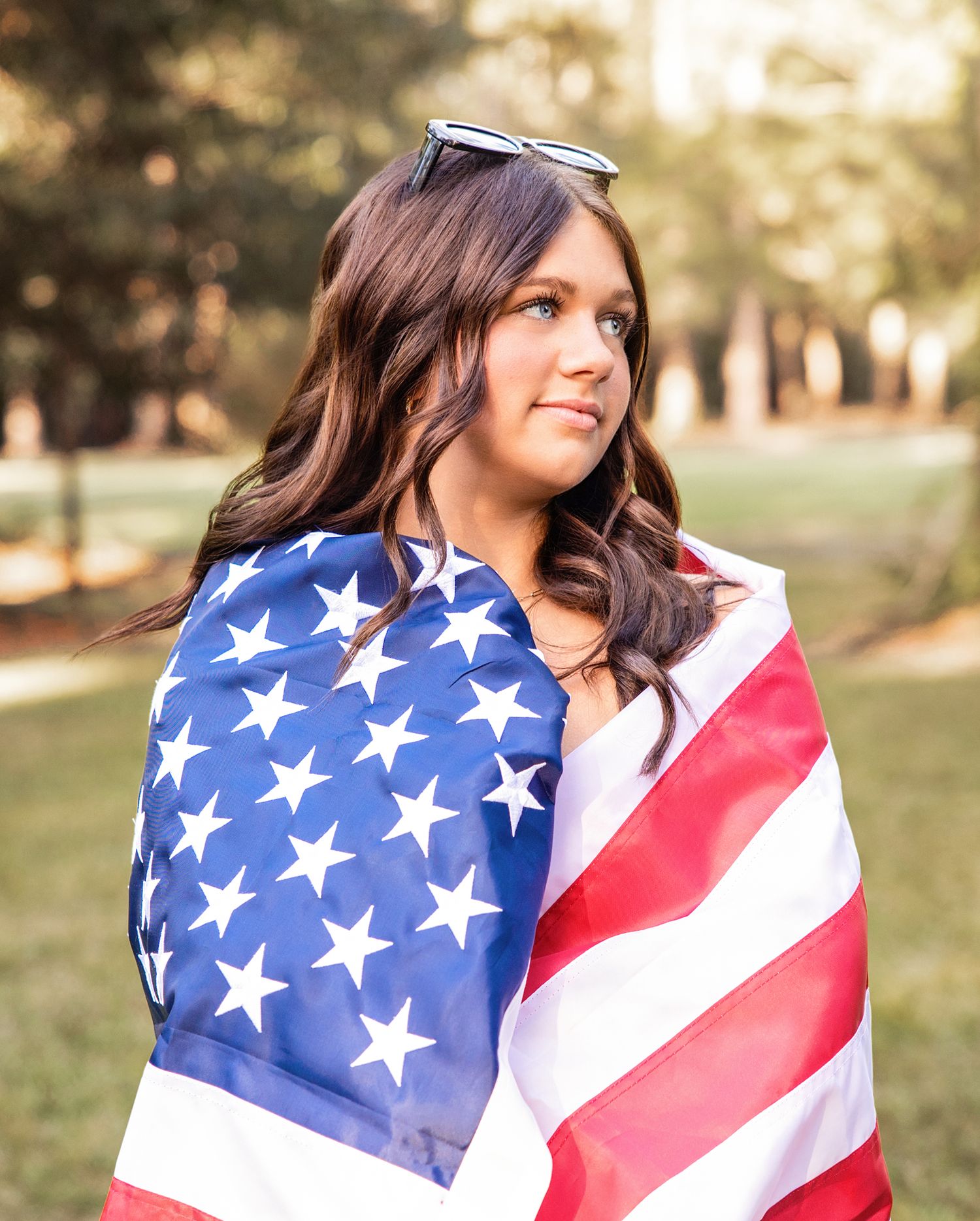 A patriotic outdoor photo session featuring someone wrapped in an American flag during golden hour.
