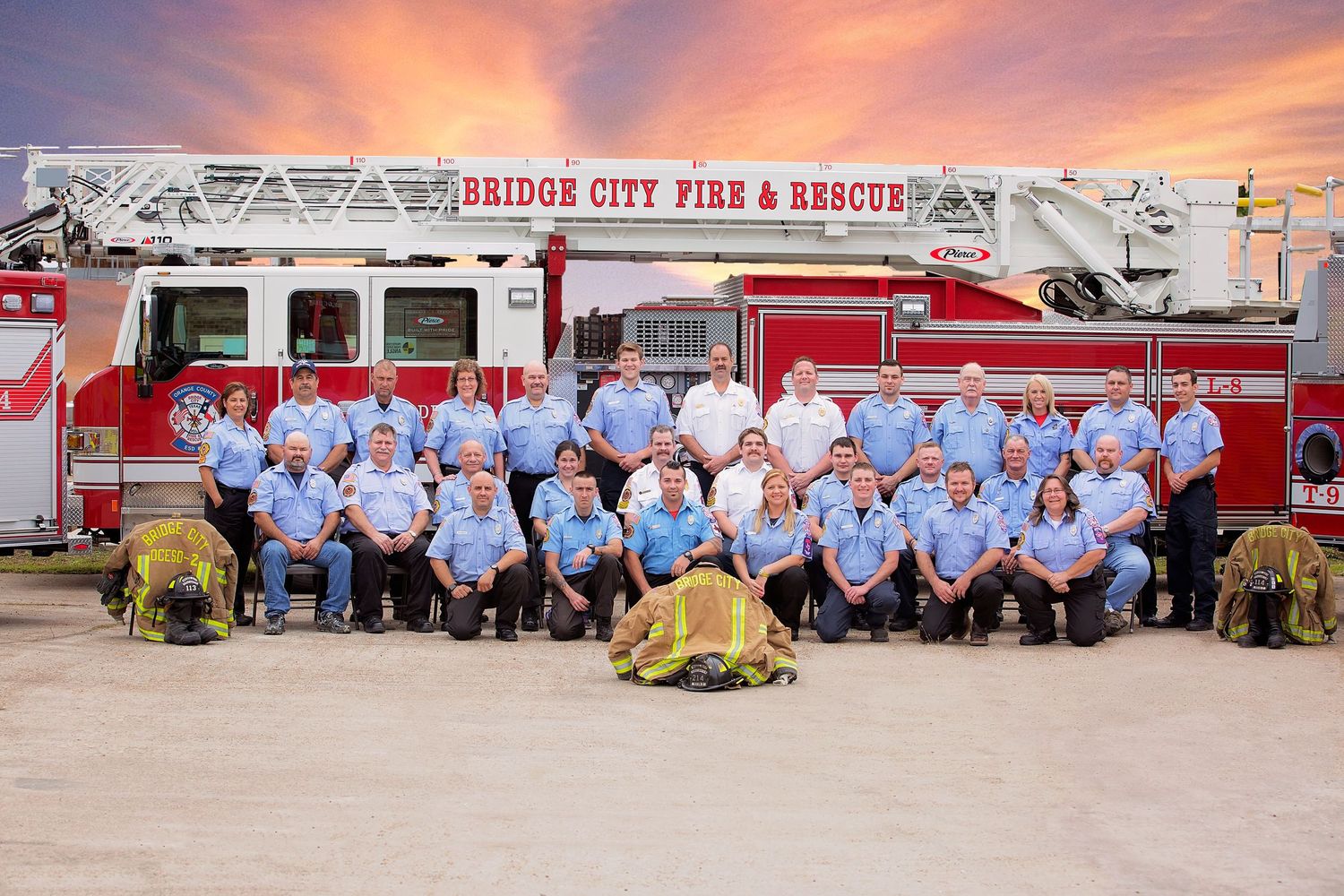 Bridge City Fire and Rescue in light blue uniforms pose in front of a red fire truck with Bridge City Fire & Rescue signage.