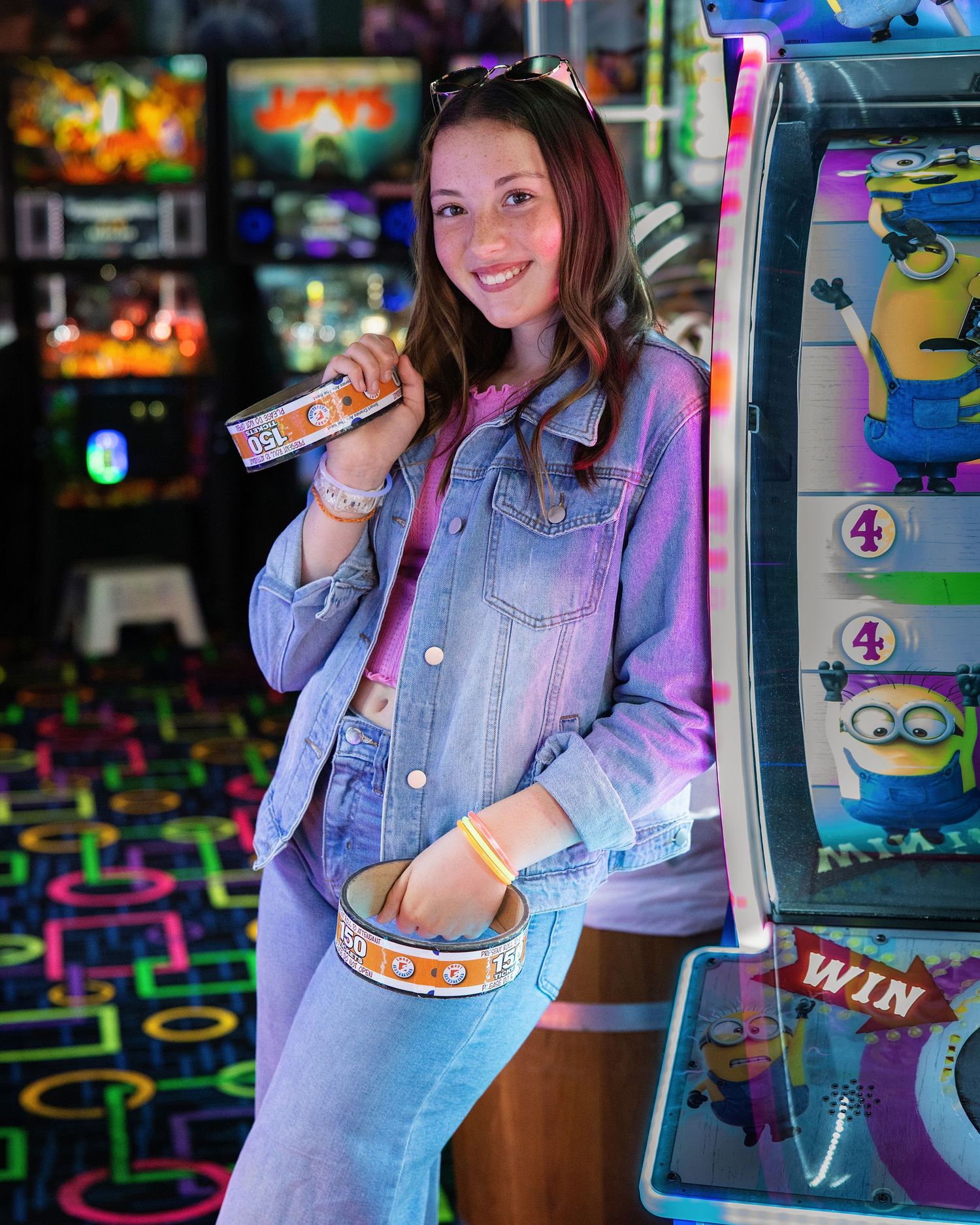 Young woman smiling in an arcade, holding tickets next to a Minions game machine.