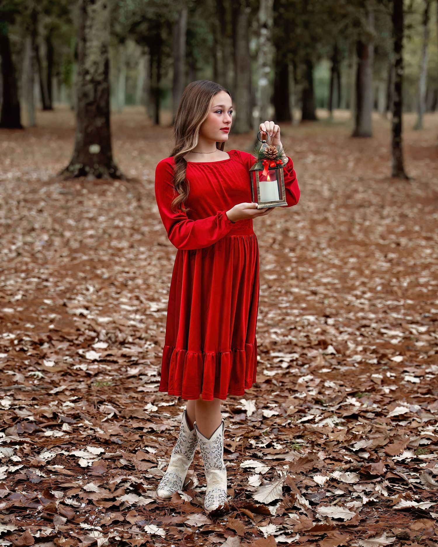 Red velvet dress styled with white boots captured in forest setting with scattered autumn leaves.