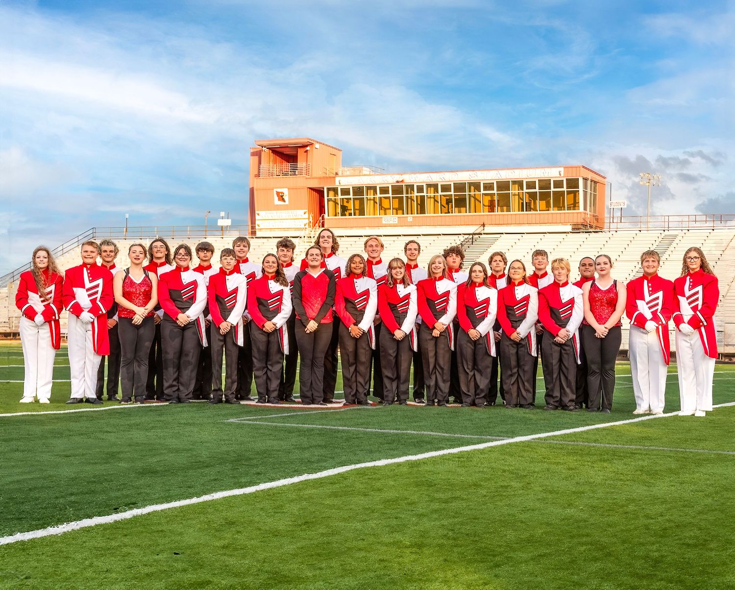 Soccer team players lined up on a green field against a bright blue sky during a pre-match ceremony.