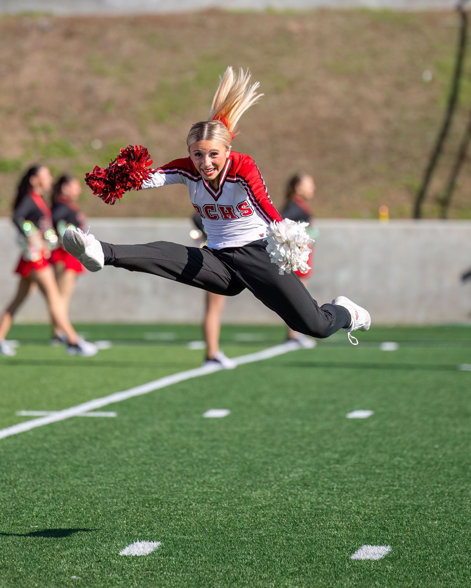 A cheerleader executing an impressive aerial jump with pom poms on the football field.