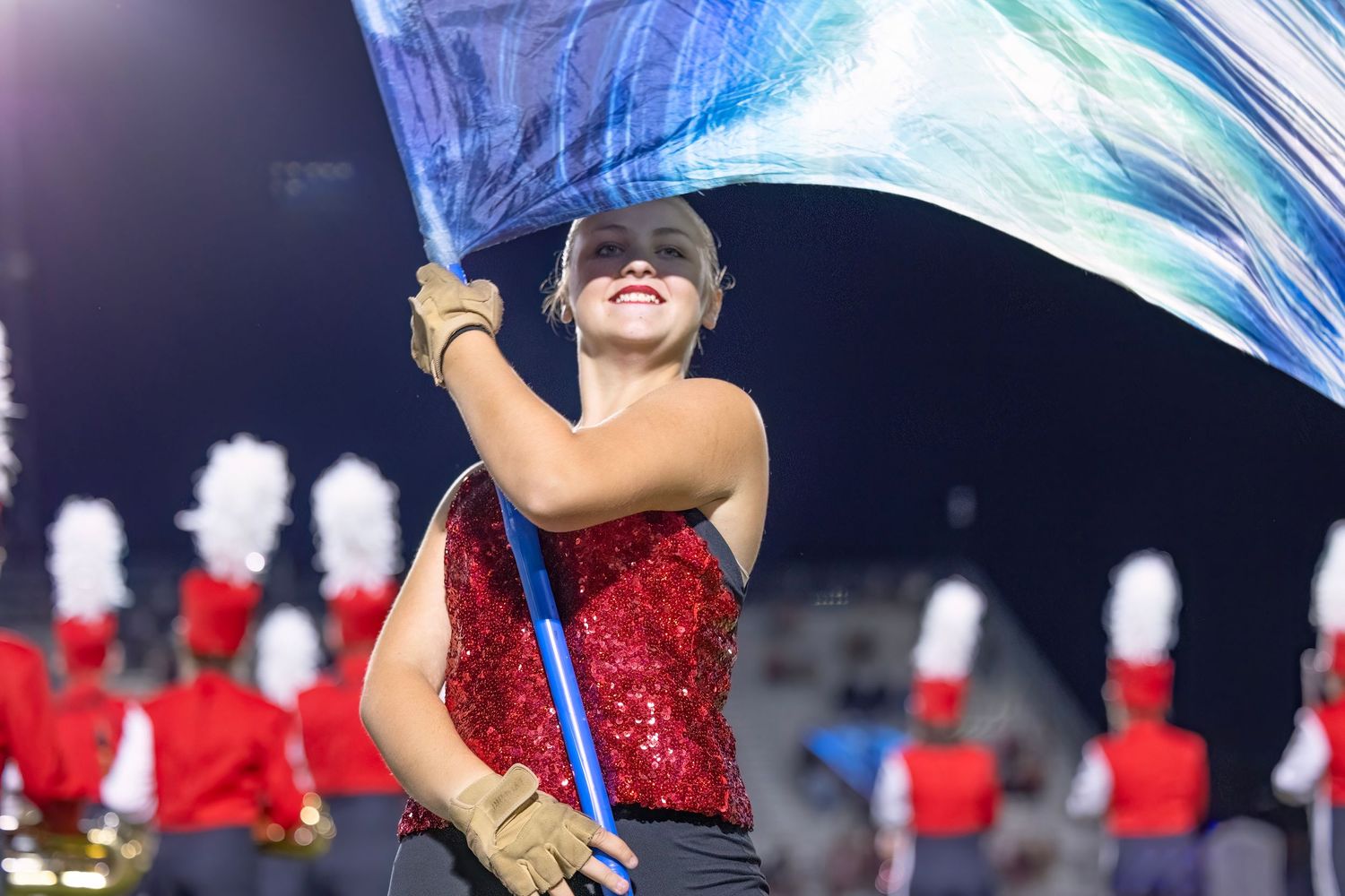 Cheerleaders in sparkly red uniforms perform a dance routine under stadium lights.