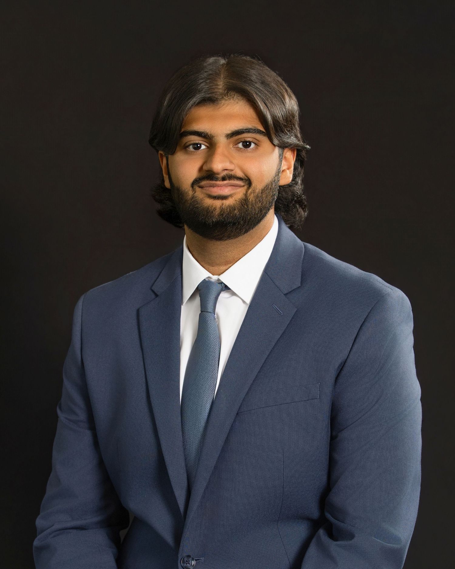 Professional headshot portrait of someone in a navy suit and white tie against a dark background.