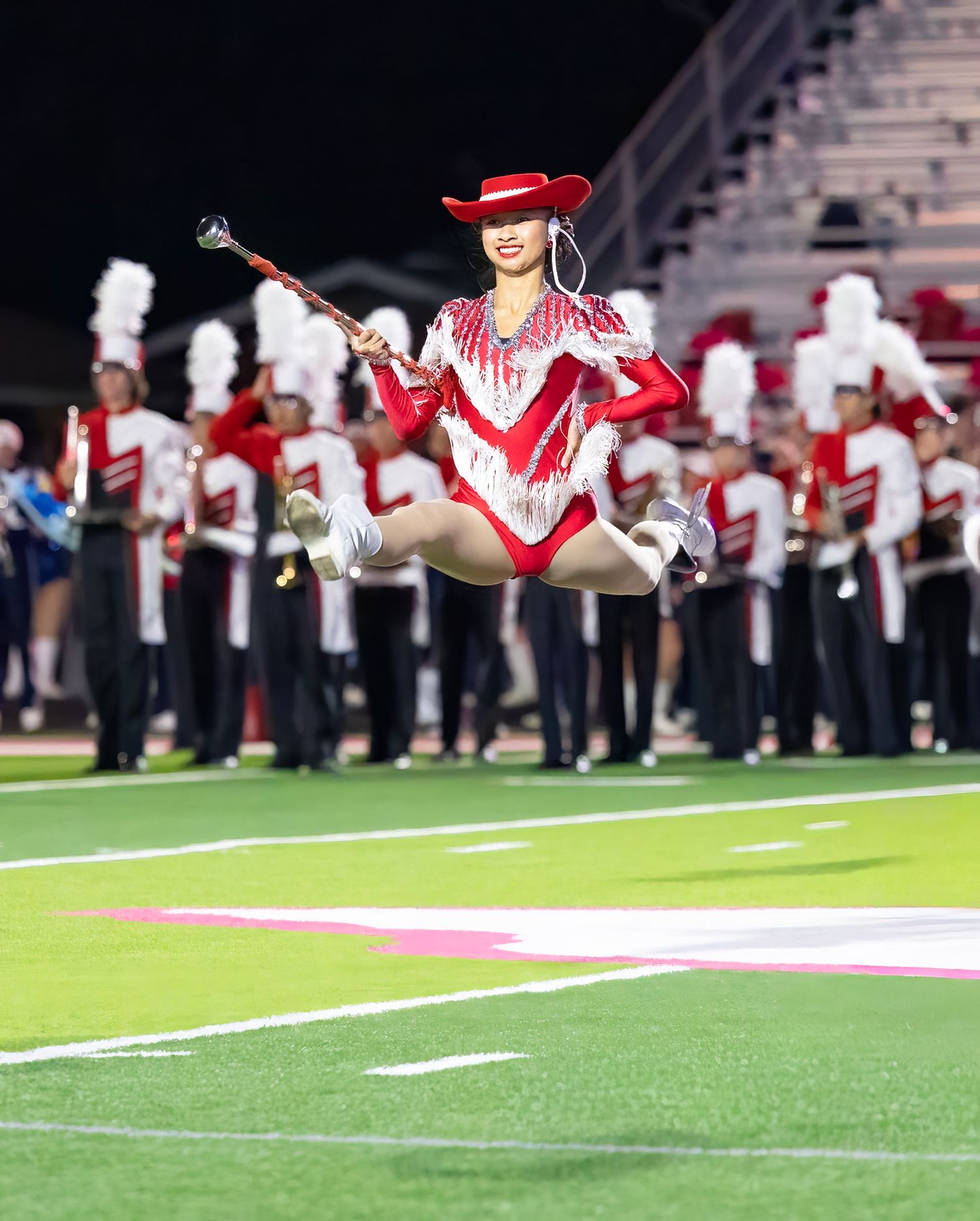 Marching band plays for the BC Strutters in a synchronized routine on a football field during halftime.