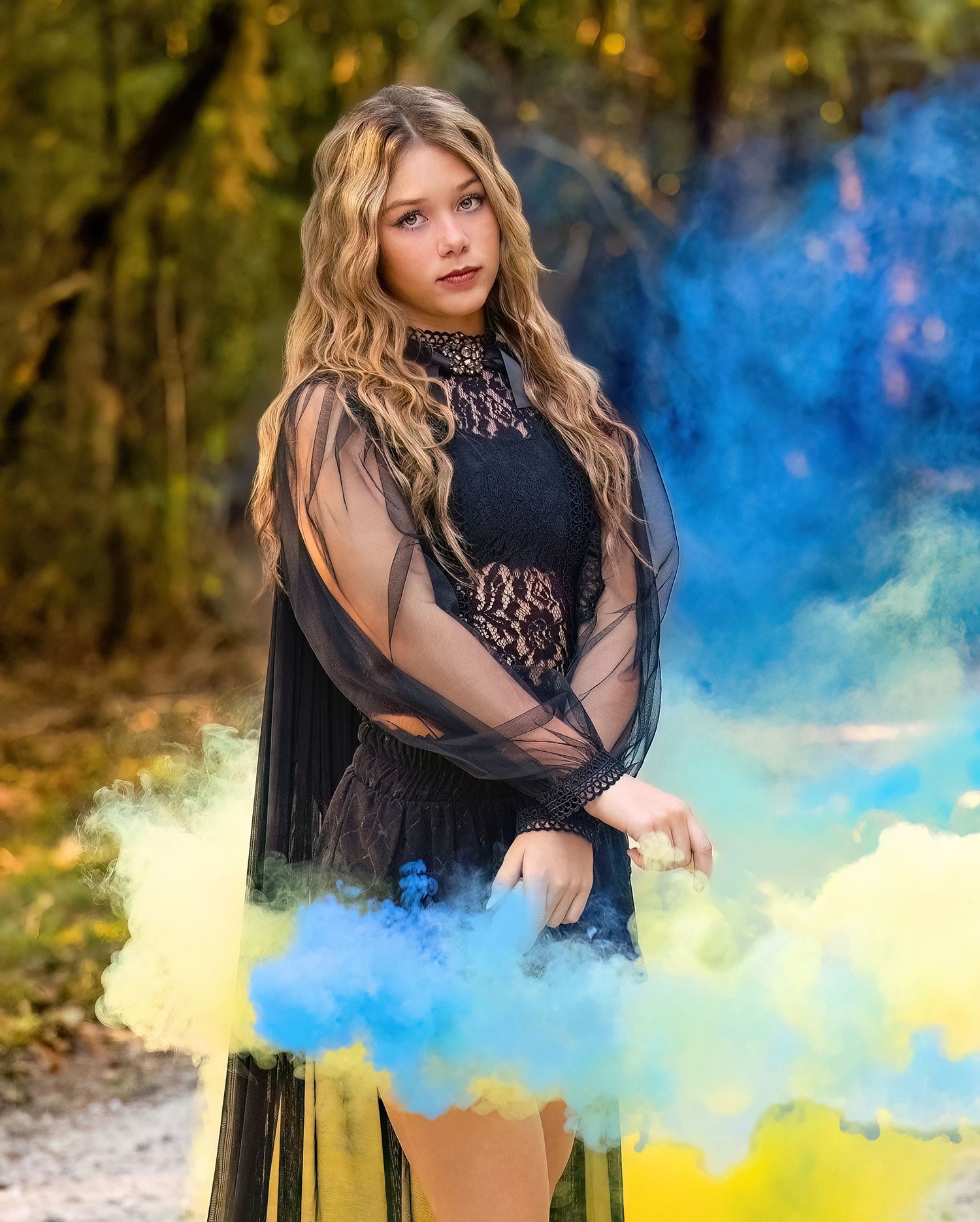 Artistic portrait with blue and yellow smoke effects in outdoor natural setting.