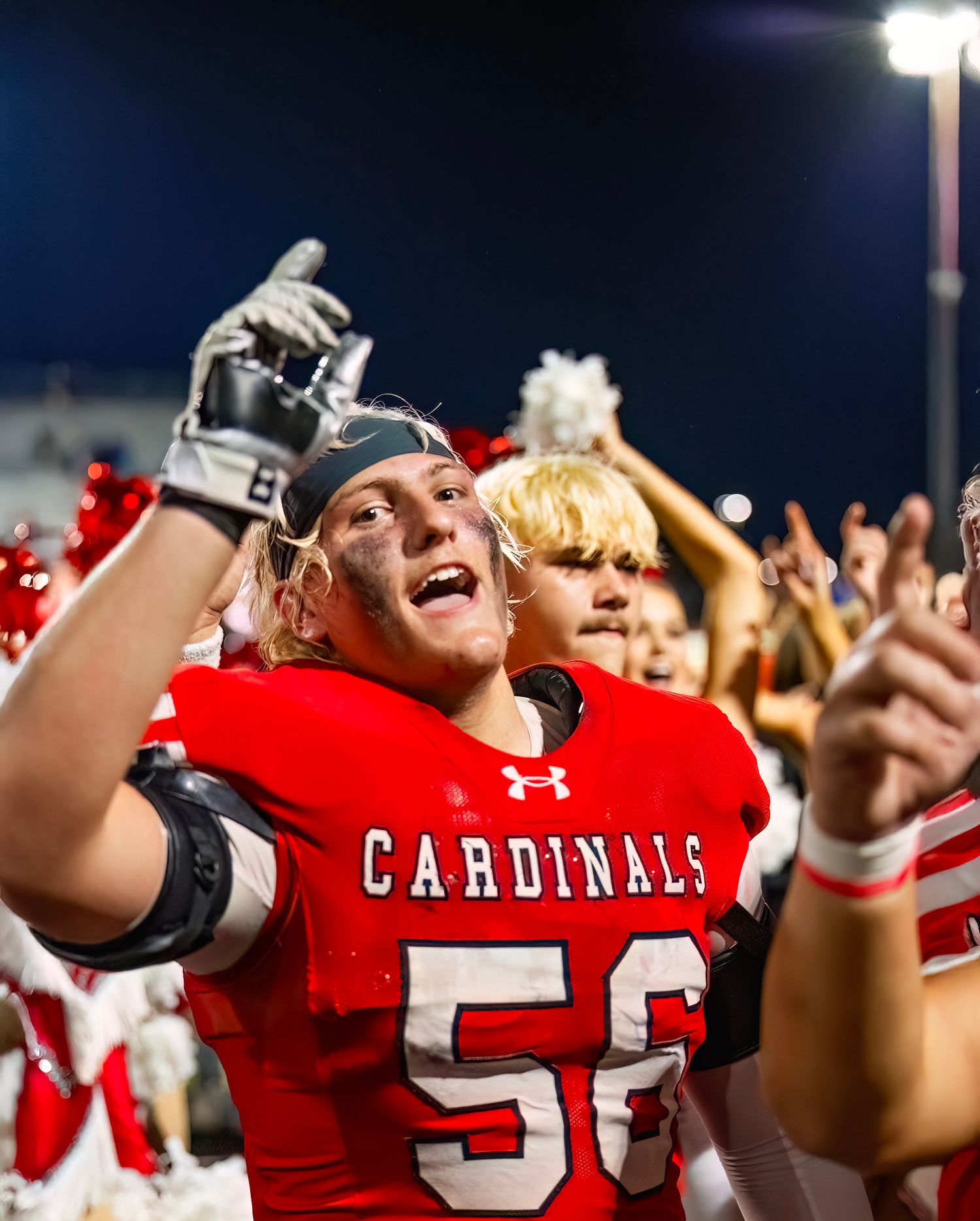 Football players in red Cardinals jerseys celebrate with excitement during a night game.