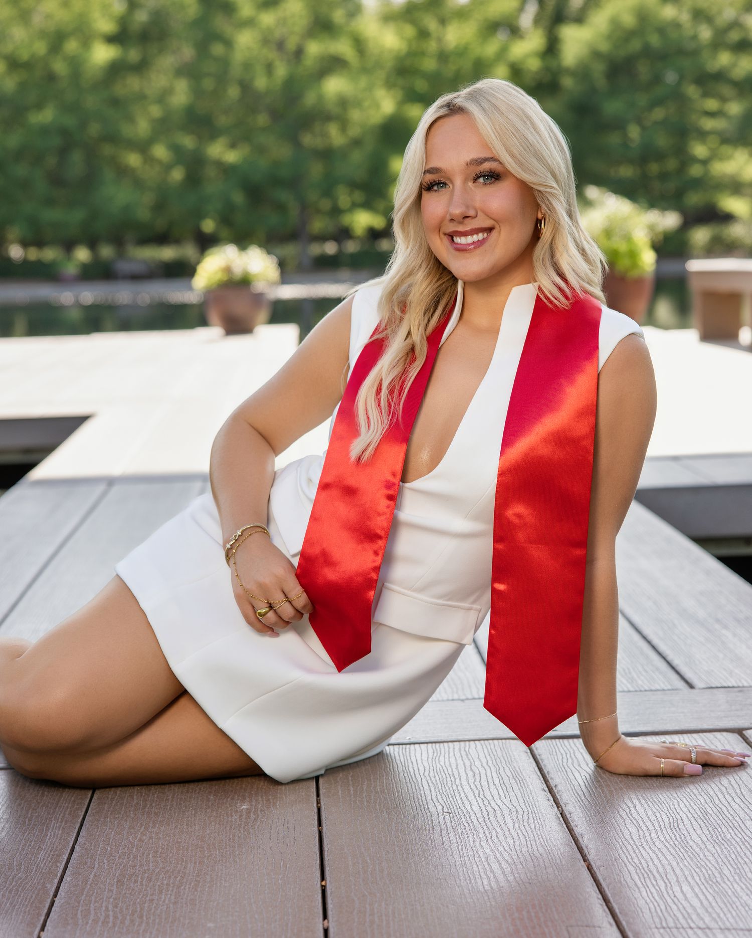 College graduation photos showing someone in a white dress and red stole posing on outdoor wooden benches.