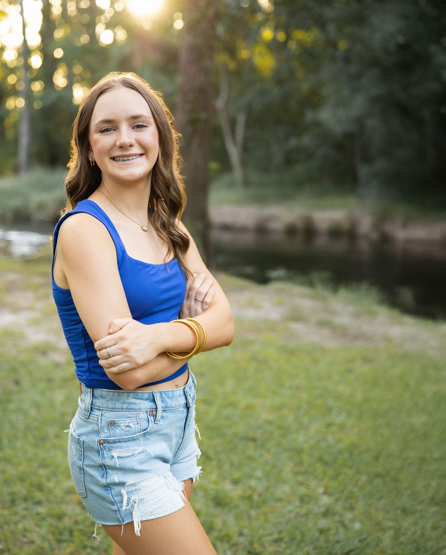 Casual outdoor portrait featuring someone in a blue tank top and denim shorts posing playfully.