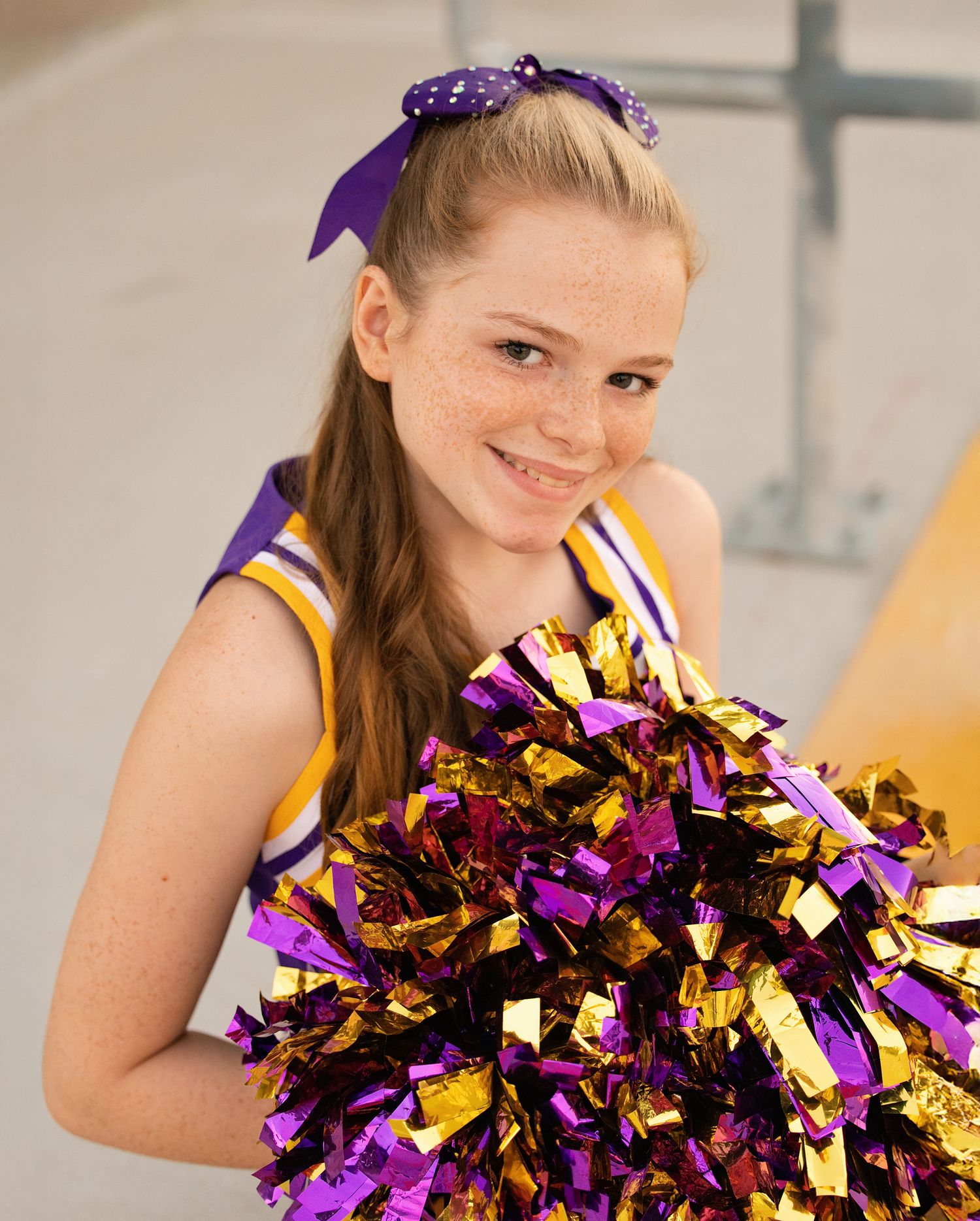Cheerleader with purple and gold pom poms performs during indoor event.