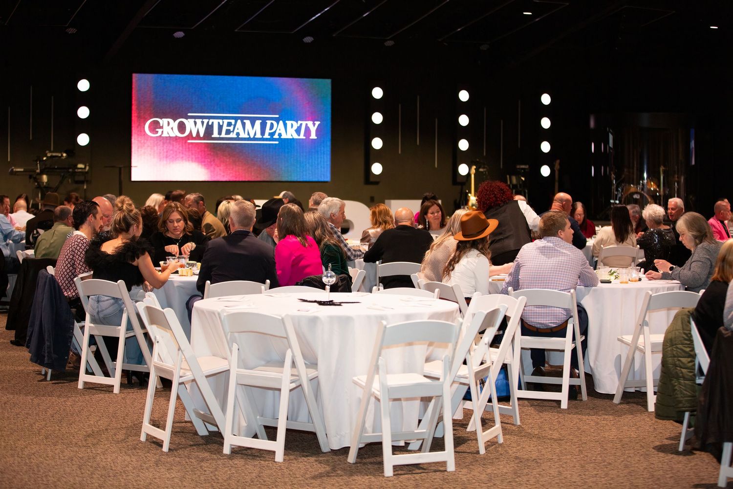 Corporate event with Round banquet tables with white tablecloths and chairs set up in a dimly lit event space for a formal gathering.