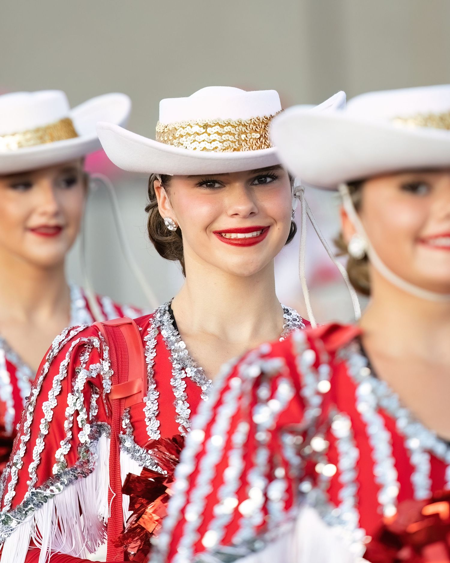 A line of performers wearing matching white cowboy hats and red and white striped outfits at an outdoor event.