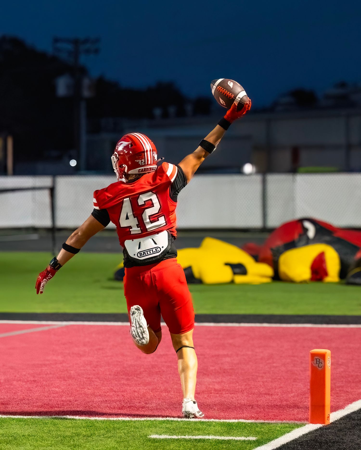 Football player in red jersey leaps towards the end zone during a touchdown attempt.