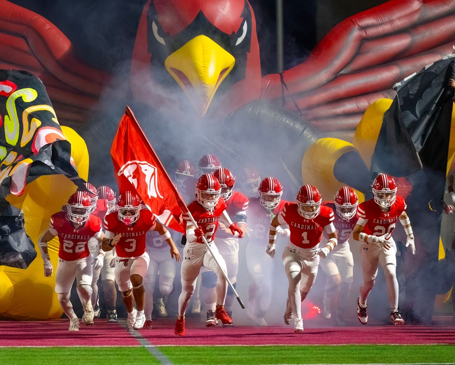 Football players in red and white uniforms emerge through dramatic smoke during a game entrance.