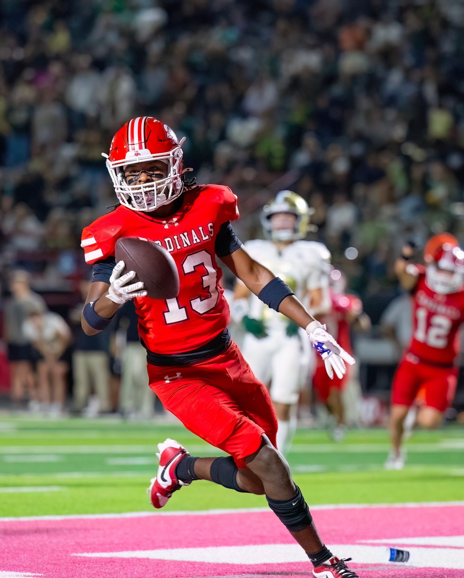 Football player in red uniform diving towards the end zone during an intense game play.