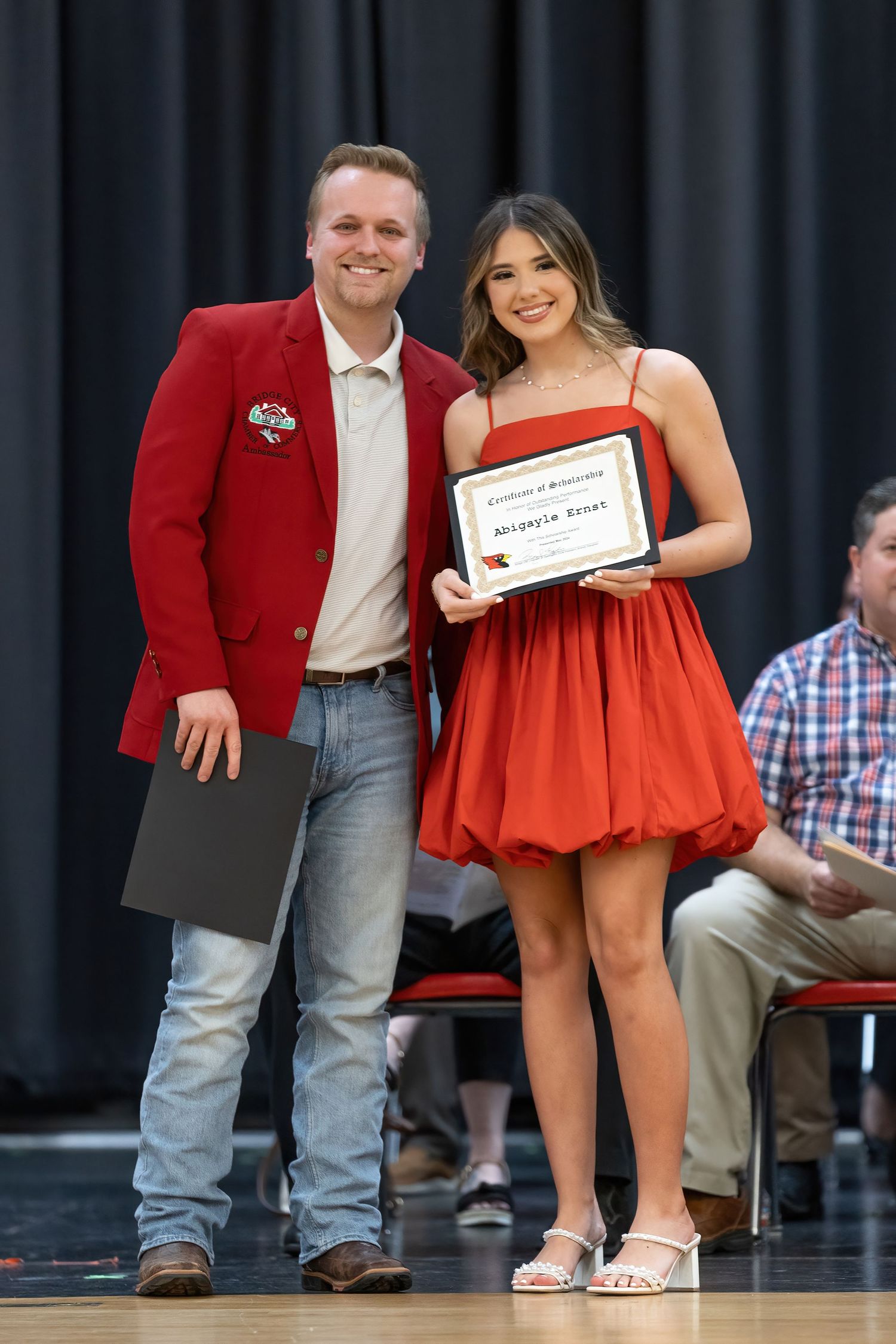 Bridge City Scholarship event person in a red blazer and jeans stands next to someone wearing a bright red dress during an awards ceremony.