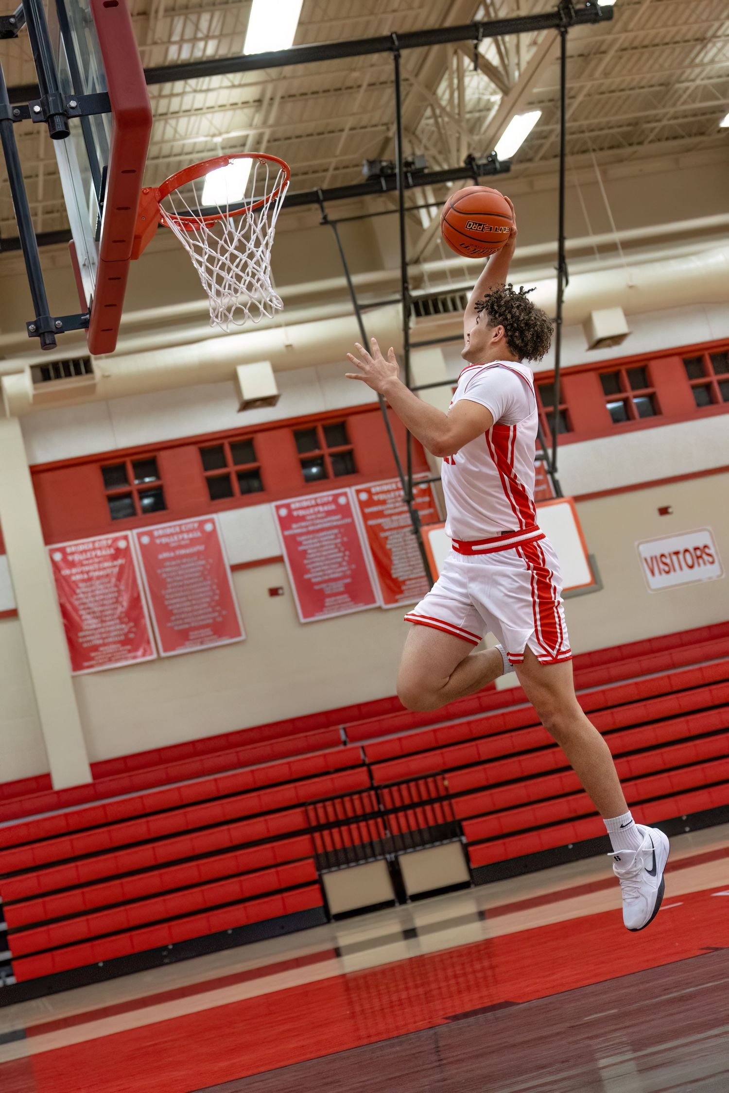 Basketball player executes a dynamic dunk sequence in a gymnasium with red bleachers and white walls.