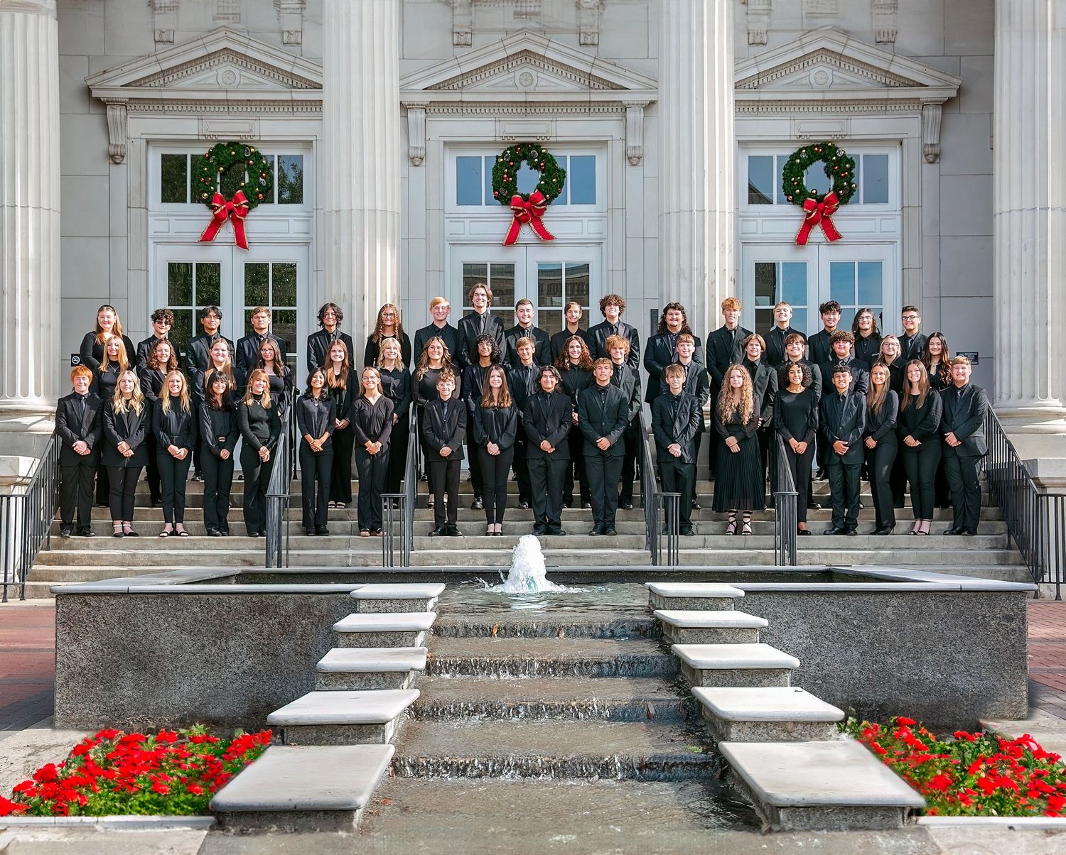 A group of people in formal attire stand on stone steps in front of a grand building with columns.
