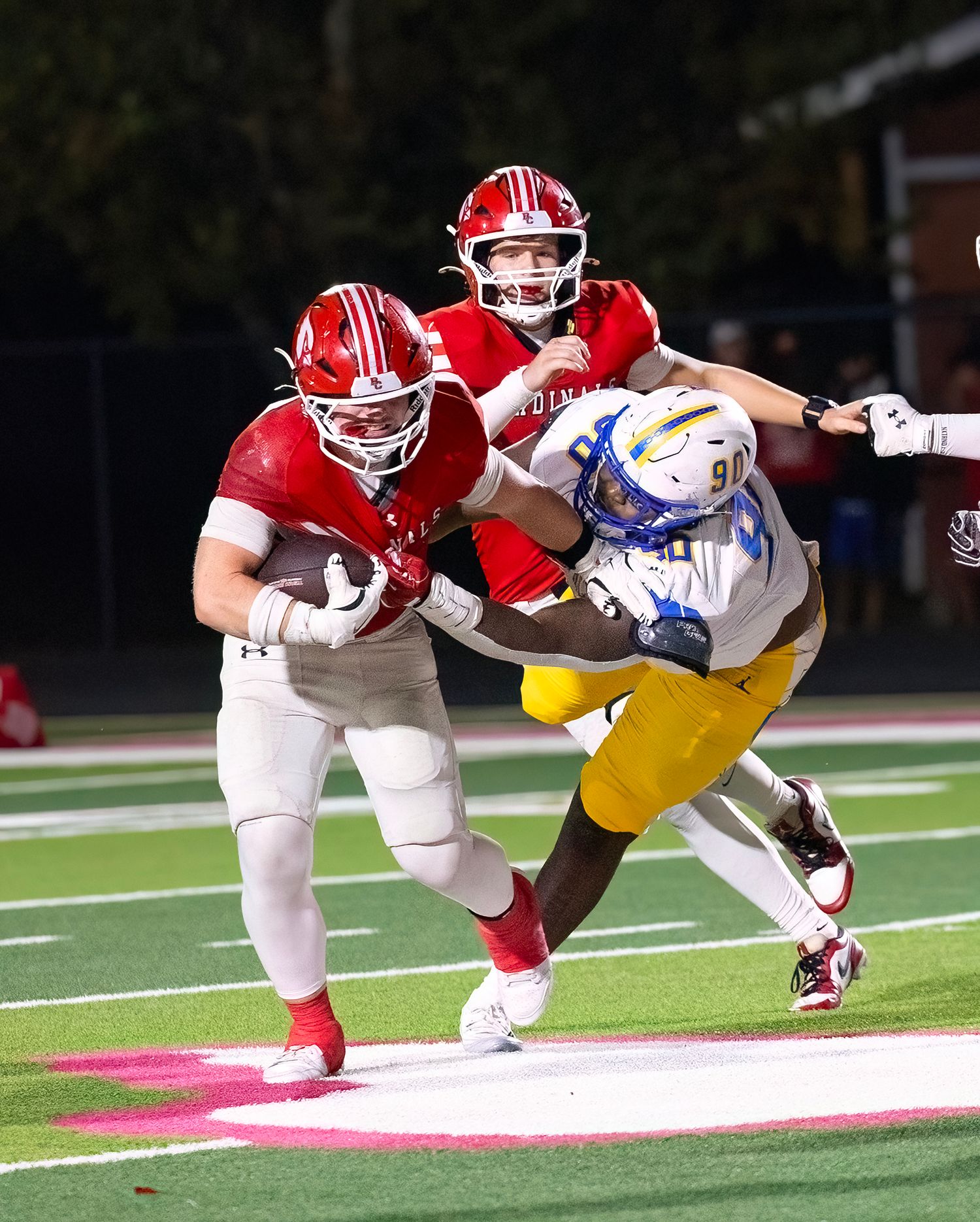 Football players in red and yellow uniforms tackle each other during an intense game play.