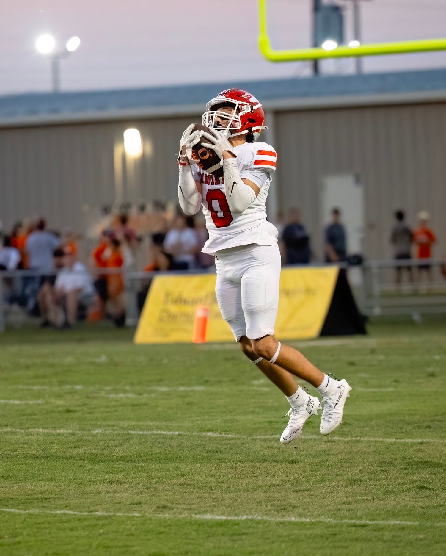 Football player in white and red uniform jumps to catch the ball during game play.