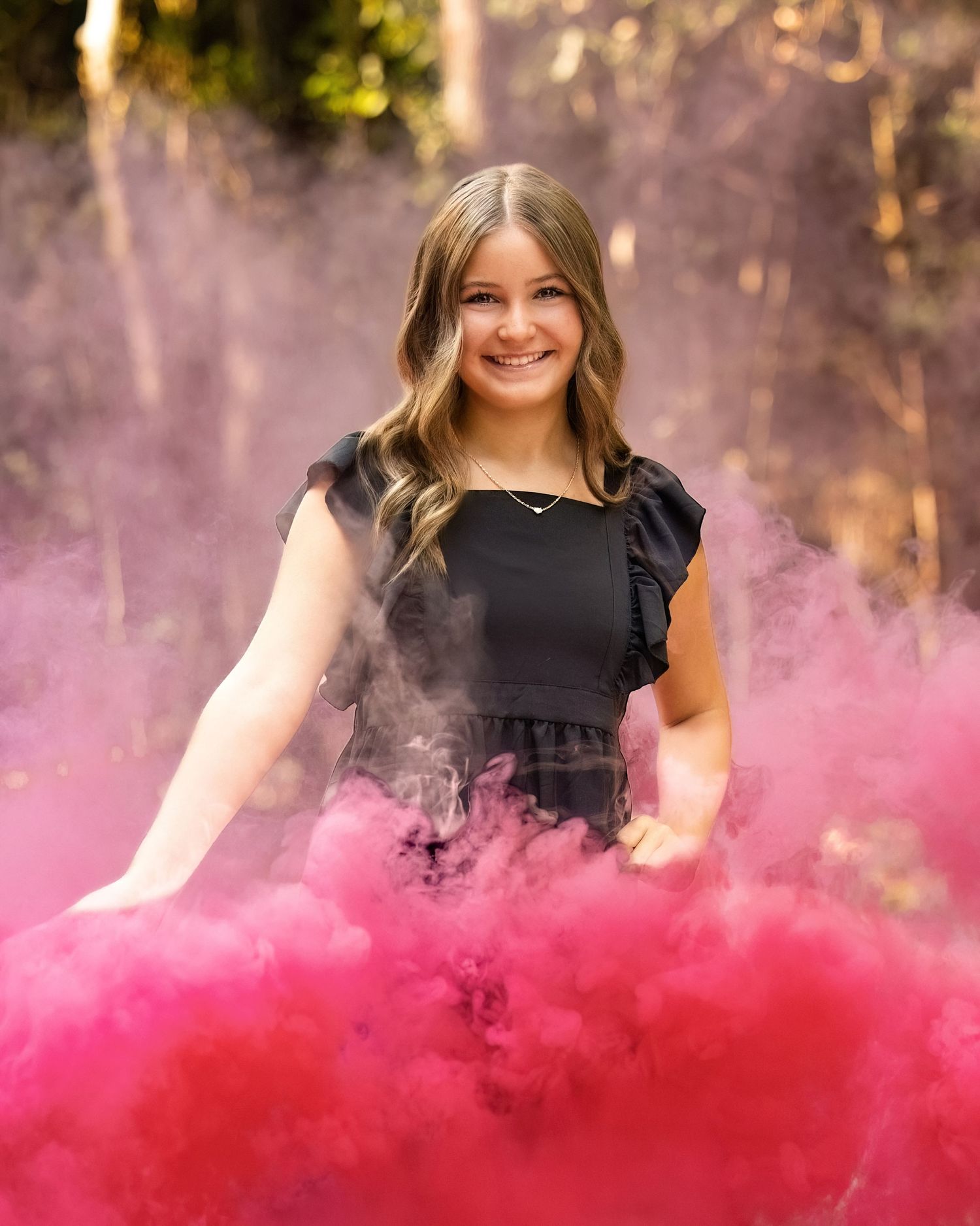 Person in black dress poses amid swirling pink smoke effect outdoors.