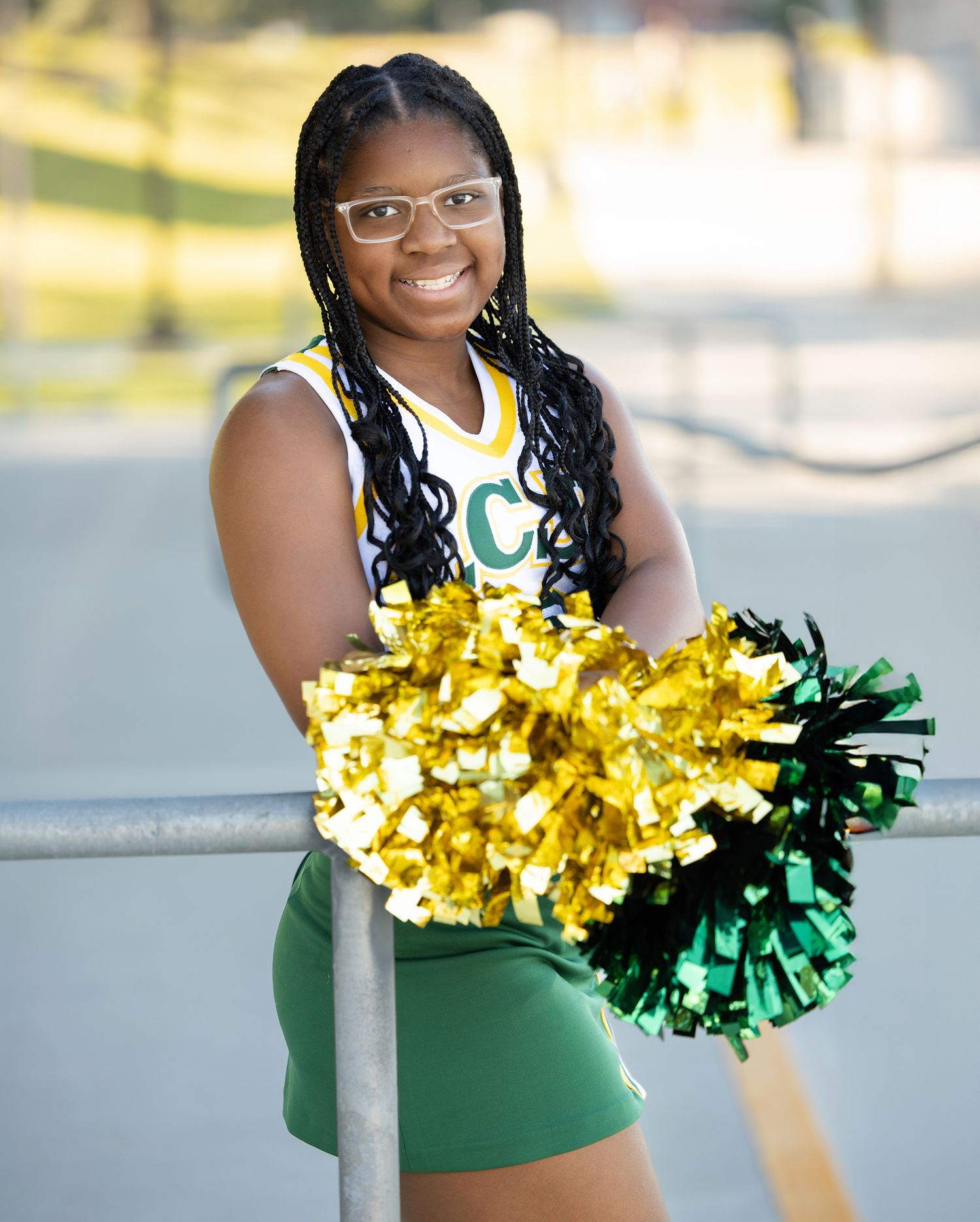 Cheerleader poses with gold and green pom poms while wearing a green and white uniform.
