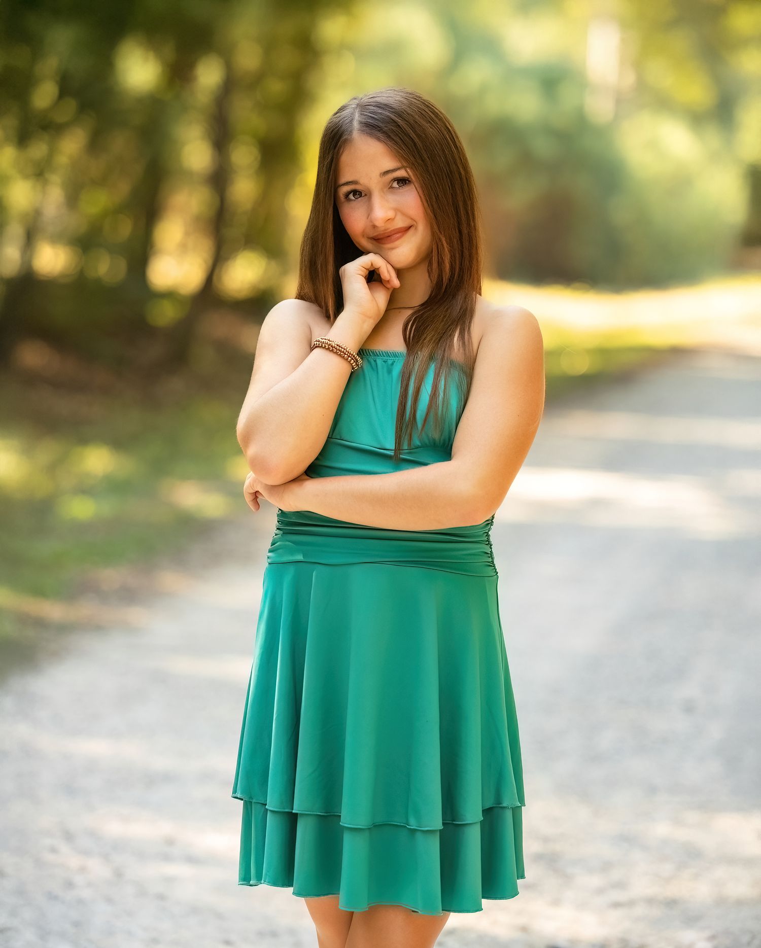 Portrait in teal layered dress standing on sunlit forest path.