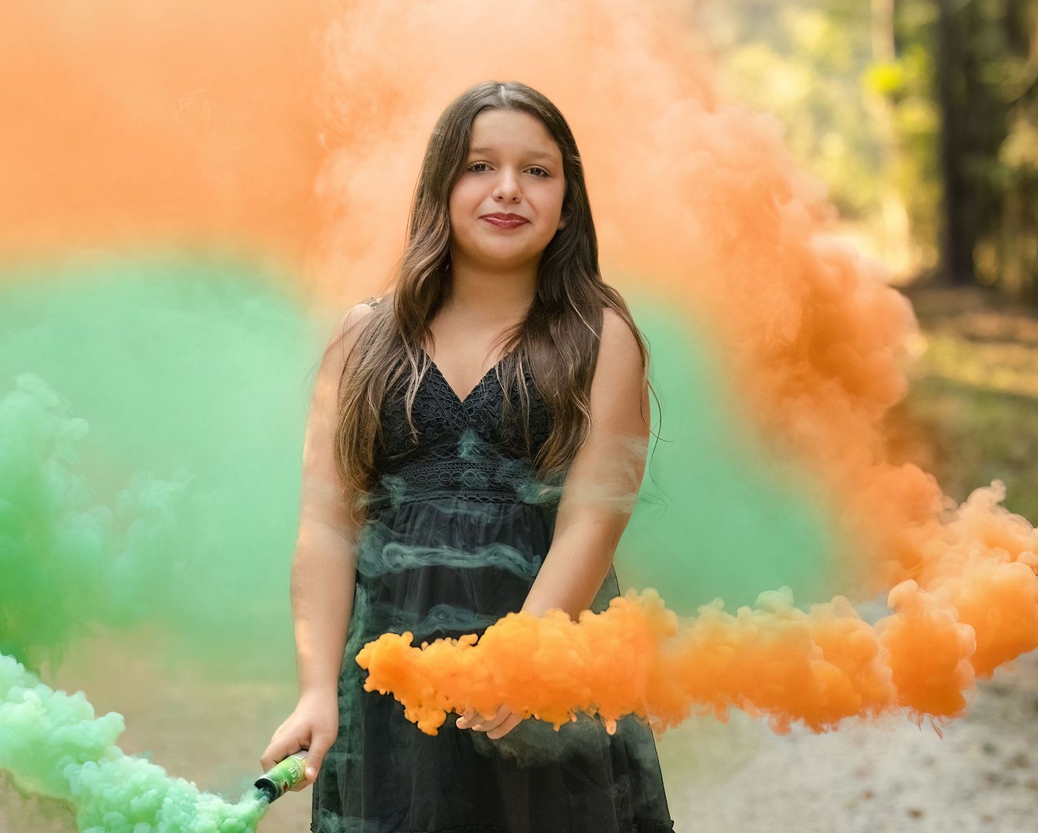 A person poses with colorful orange and green smoke bombs in an outdoor autumn setting creating a dramatic effect.