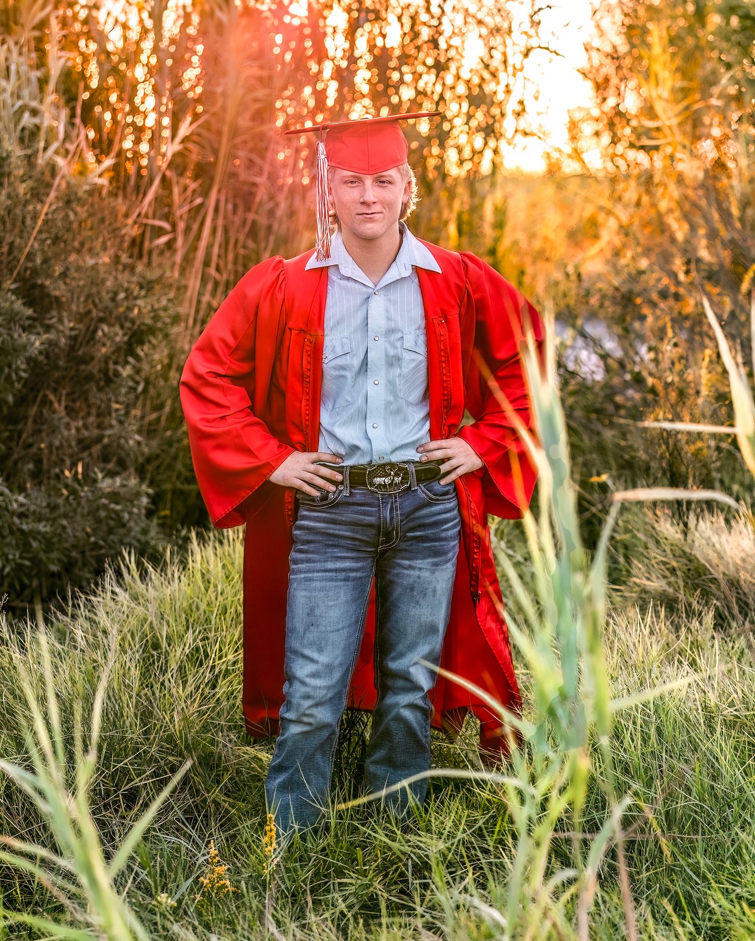 A figure in a bright red cardigan and jeans stands in tall grass during golden hour sunset.