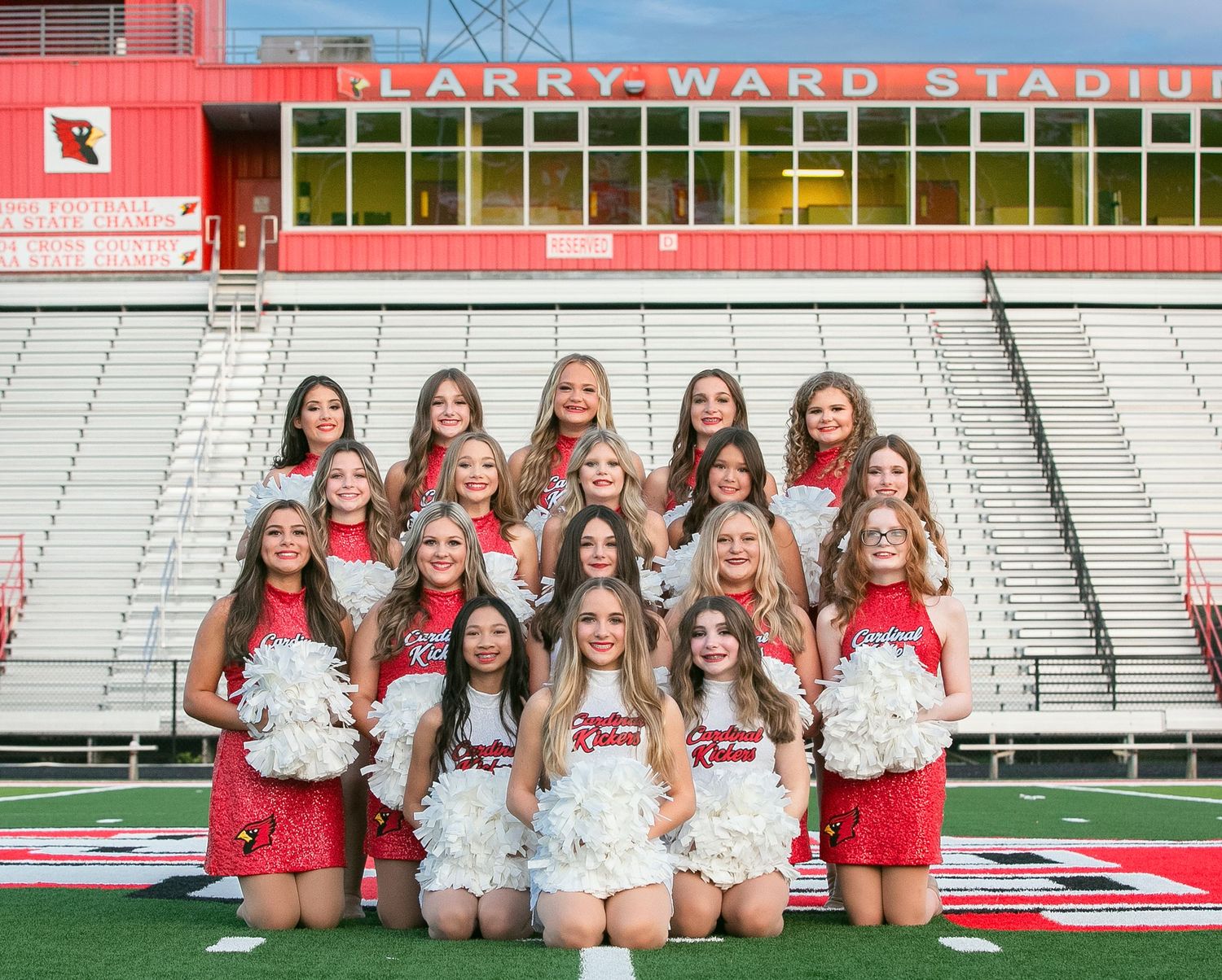 Cheerleading squad poses together on football field in red and white uniforms at Larry Ward Stadium.