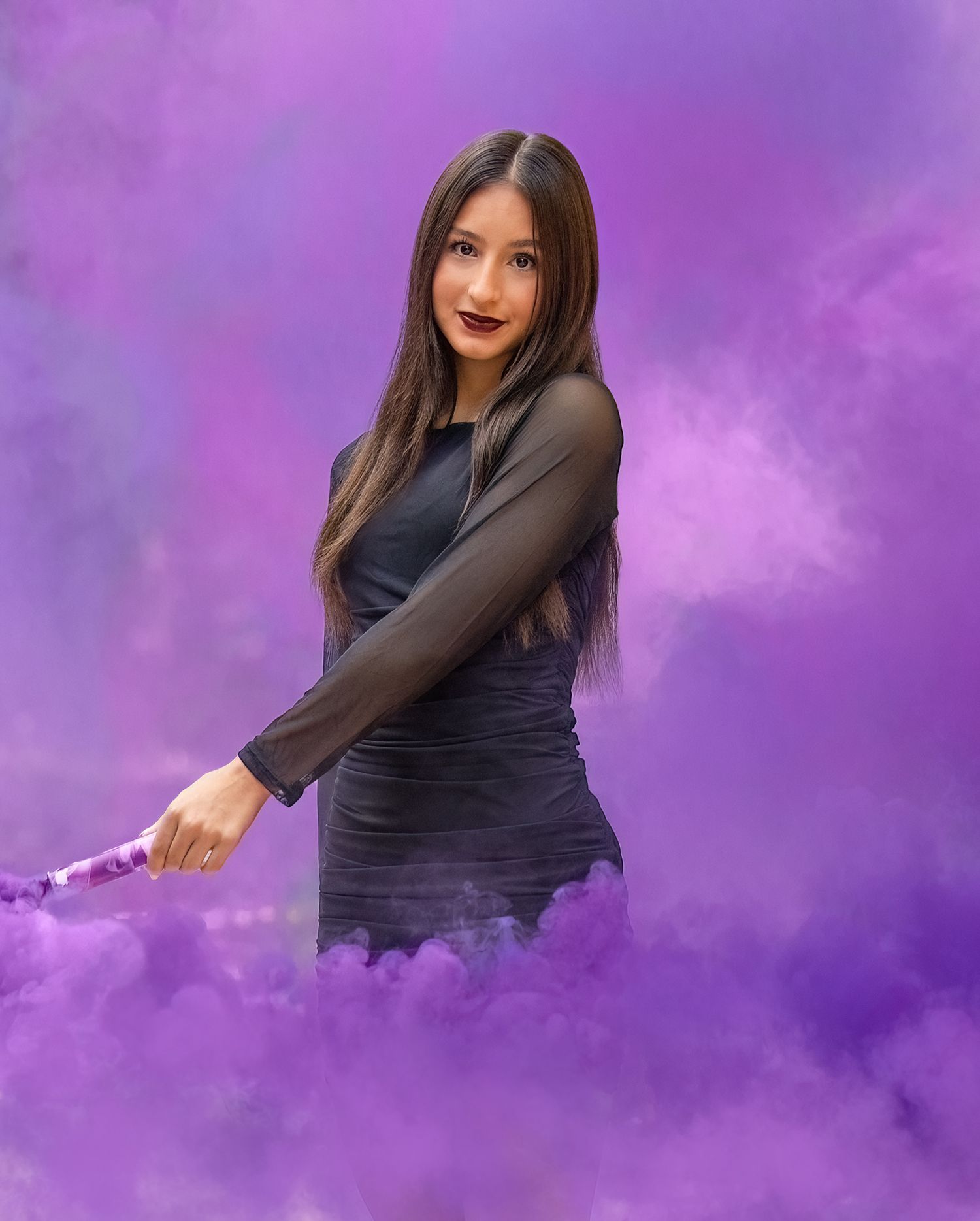Portrait against purple smoke background wearing black fitted dress.