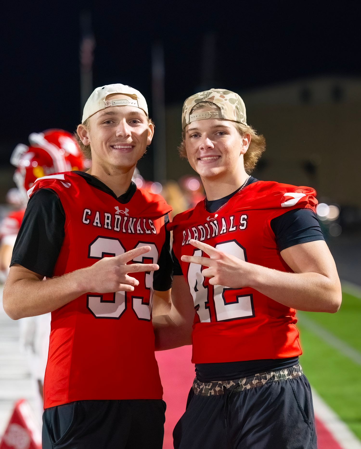 FNL Photography with Two football players in red Cardinals jerseys share a celebratory moment on the field during a game.