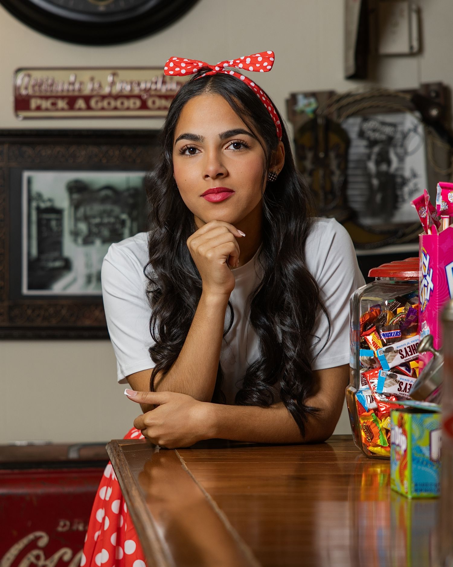 A person in a polka dot headband sits at a wooden table with colorful candy packages displayed nearby.
