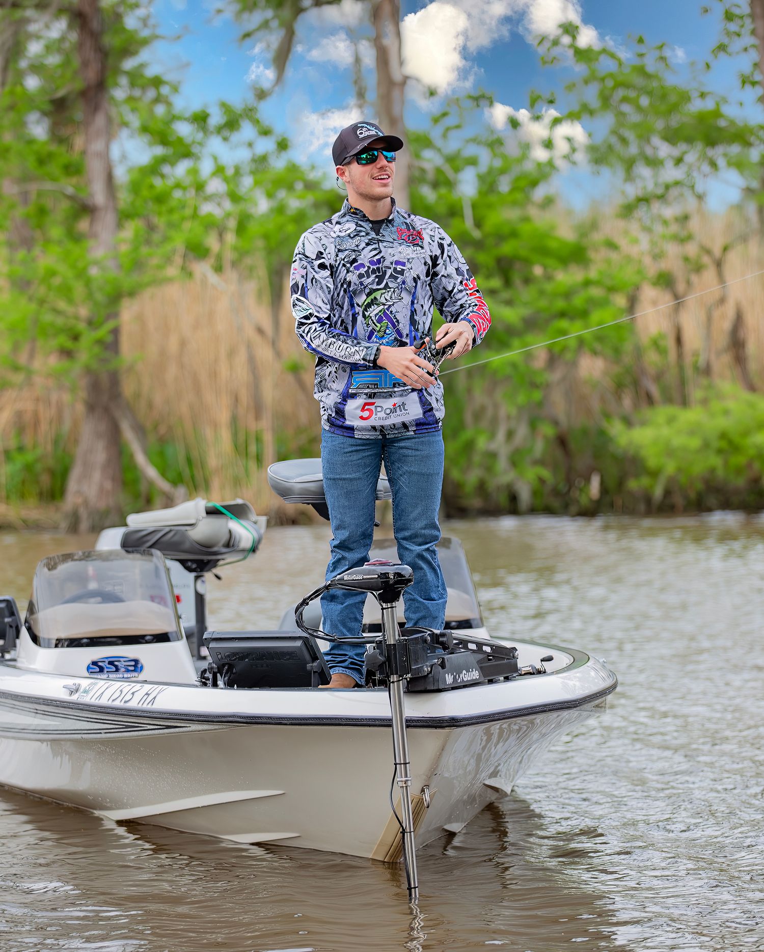 Kayak angler in a white boat fishing on a calm cypress swamp with lush green foliage in the background.