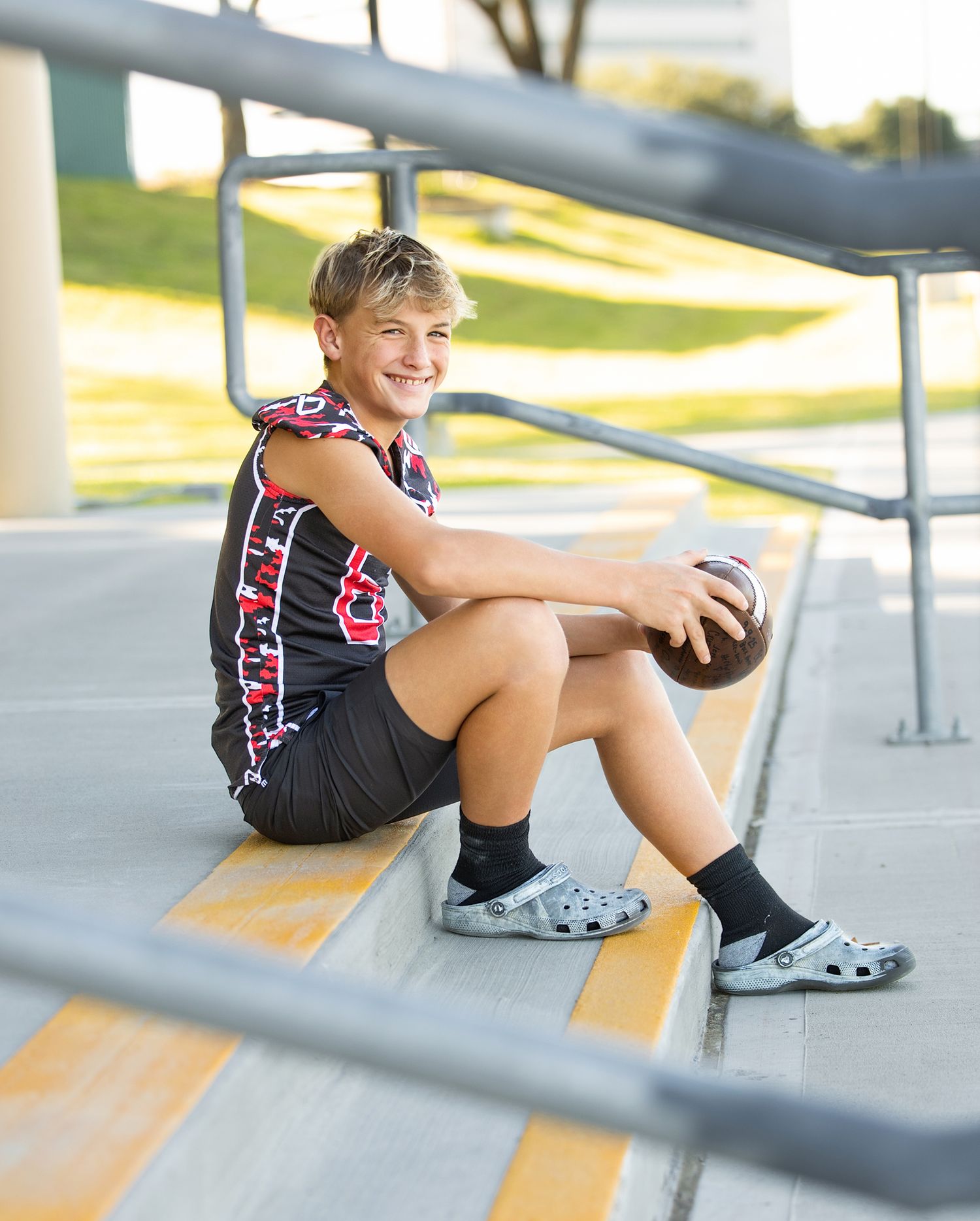 Student athlete in black and red uniform sitting on bleacher steps with volleyball.