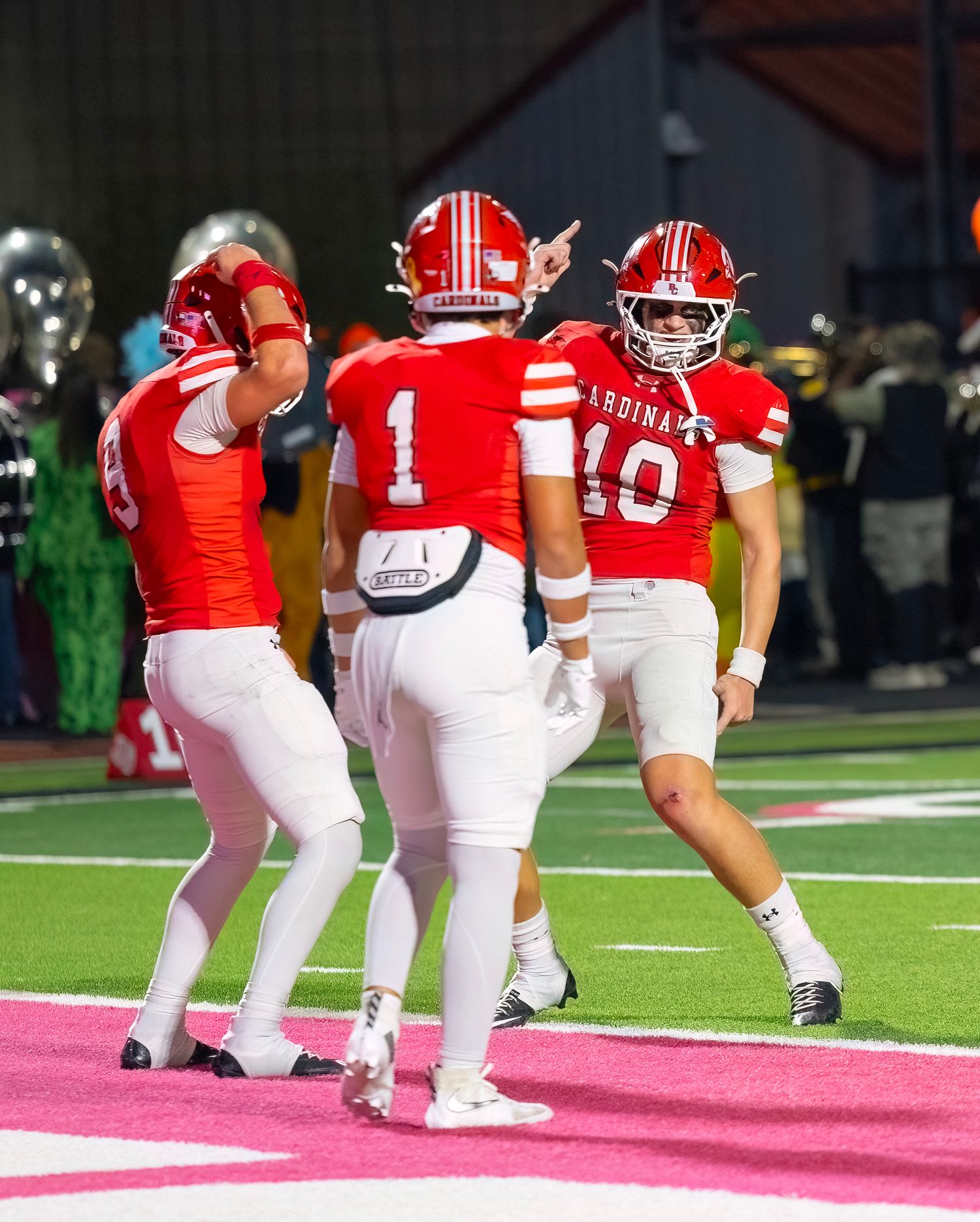 Football players in red and white uniforms line up in formation on a green playing field.