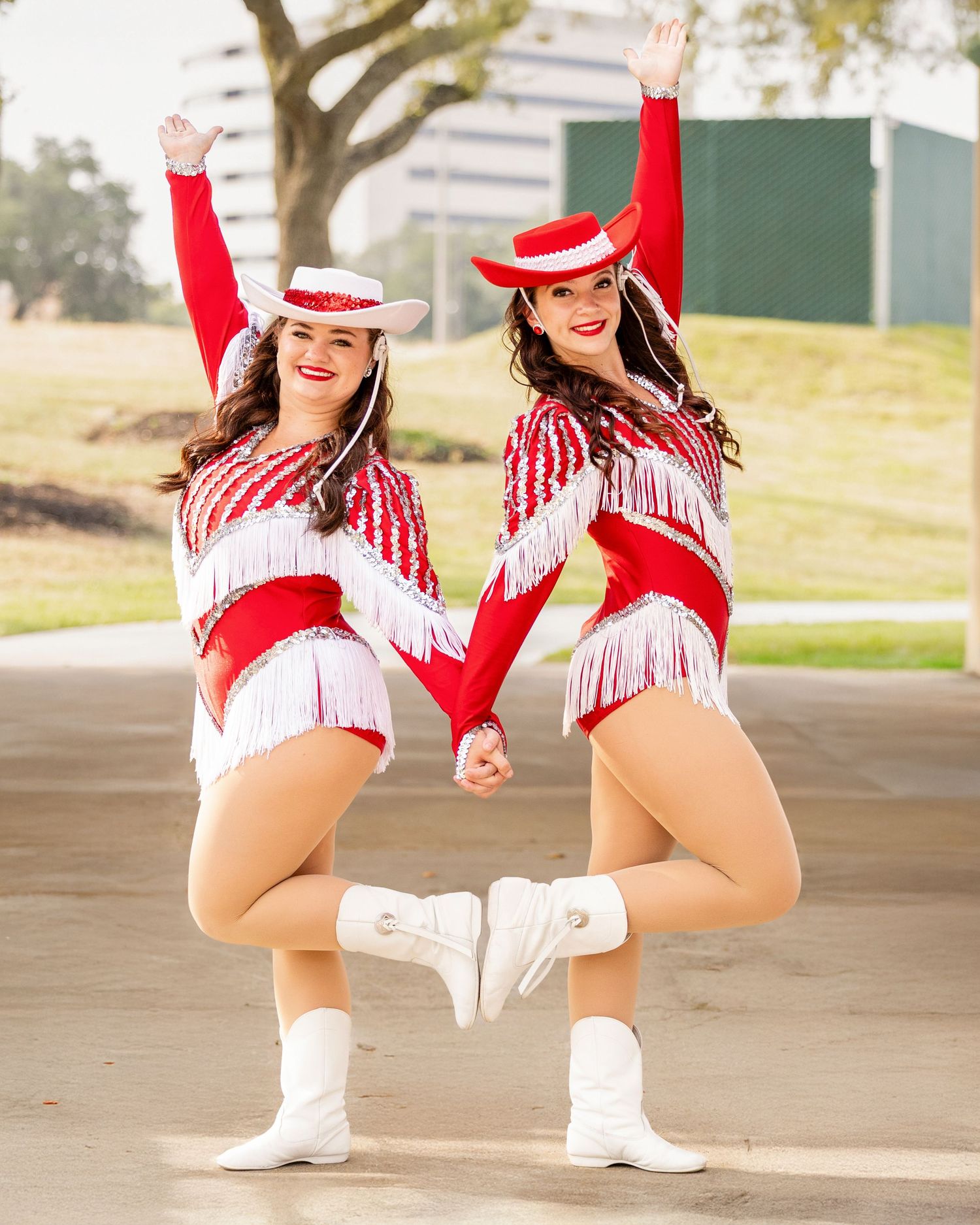 Performers in red and white costumes with matching boots strike synchronized dance poses in an outdoor setting.